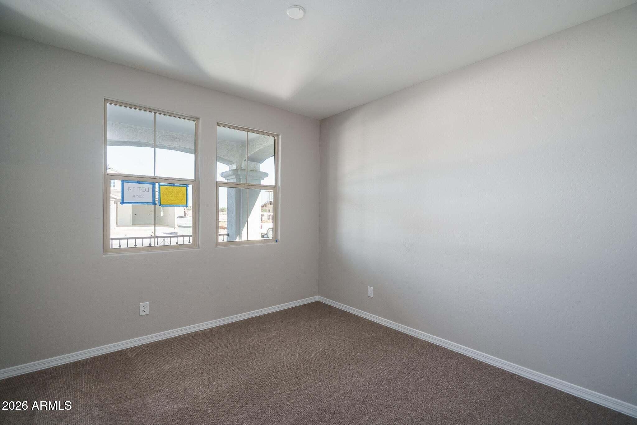 Empty carpeted room with two windows facing a covered porch.
