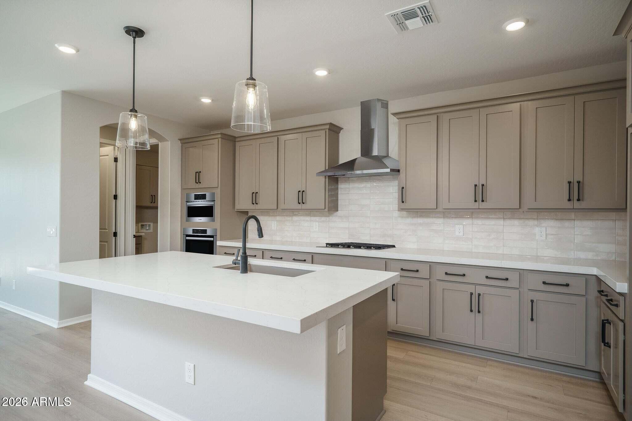 Kitchen with a large white island, taupe cabinets, double ovens, and a stainless range hood.