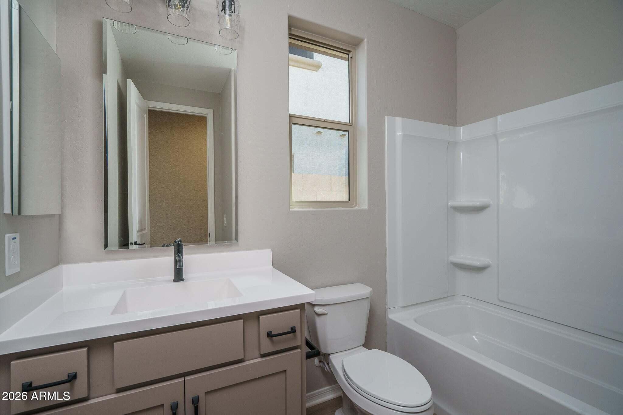 Bathroom with a wide vanity, large mirror, and tub-shower beside a tall window.