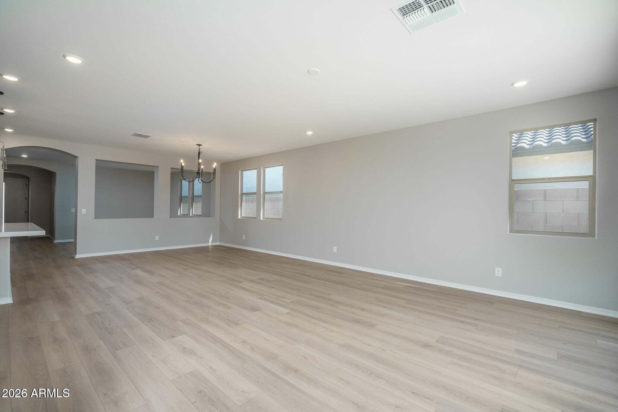 Vacant living and dining area with light wood-look floors, a black chandelier, and multiple windows.