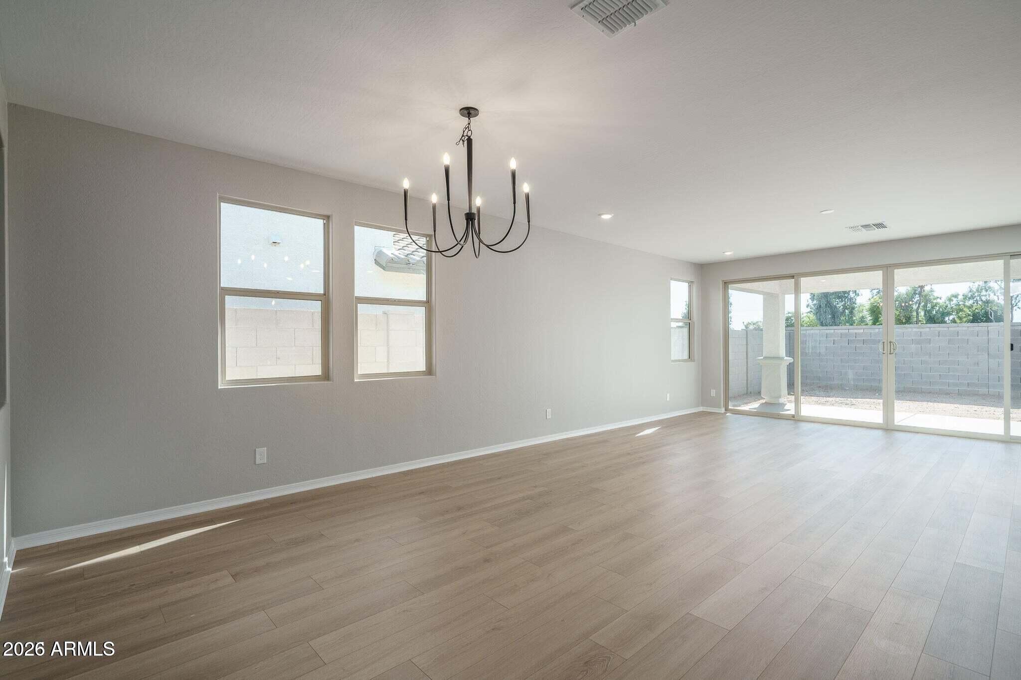 Empty dining area with wood-look floors, a black chandelier, and sliding glass doors to the backyard.