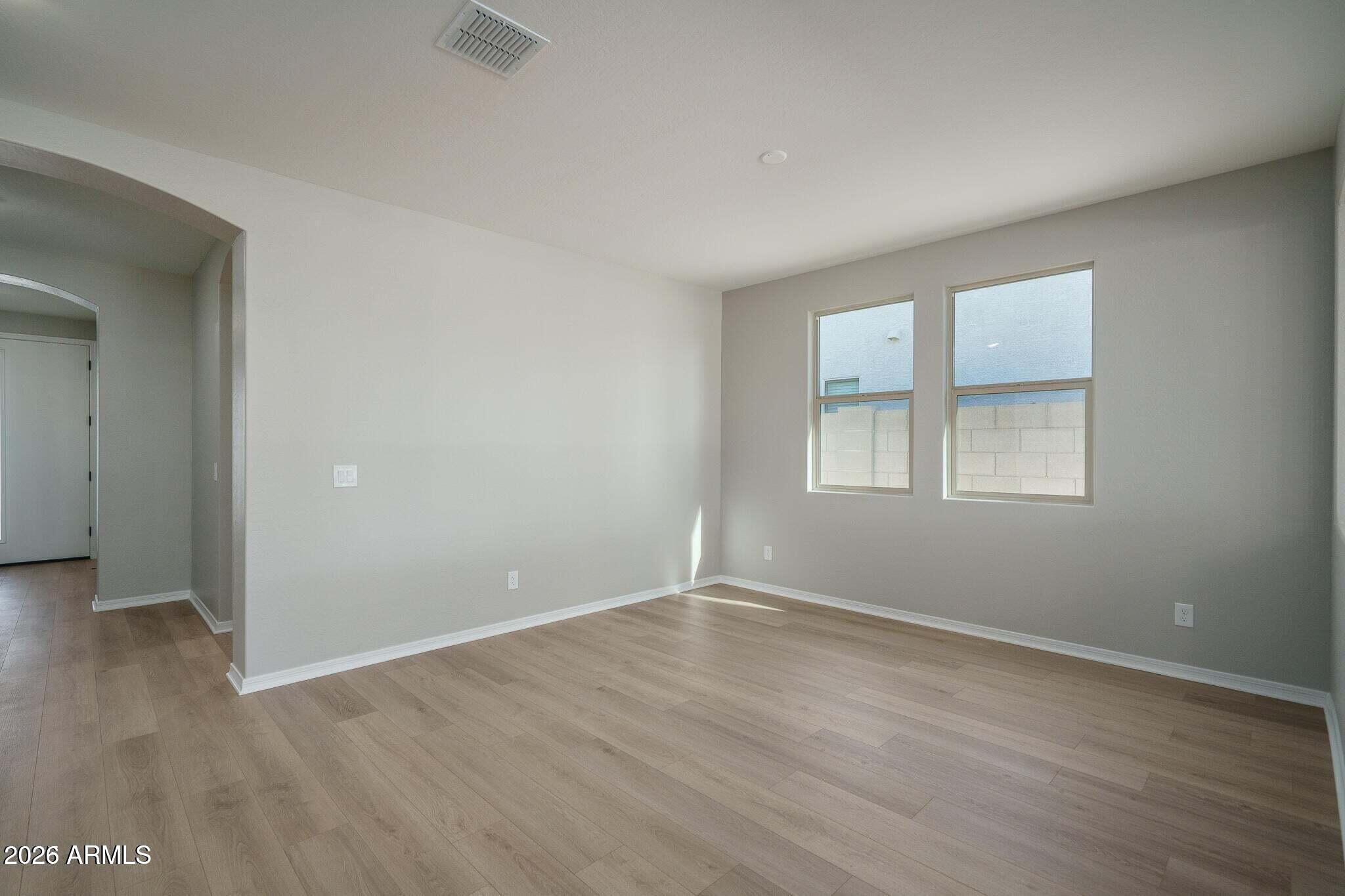 Vacant living area with light plank flooring, two windows, and an arched hallway opening.