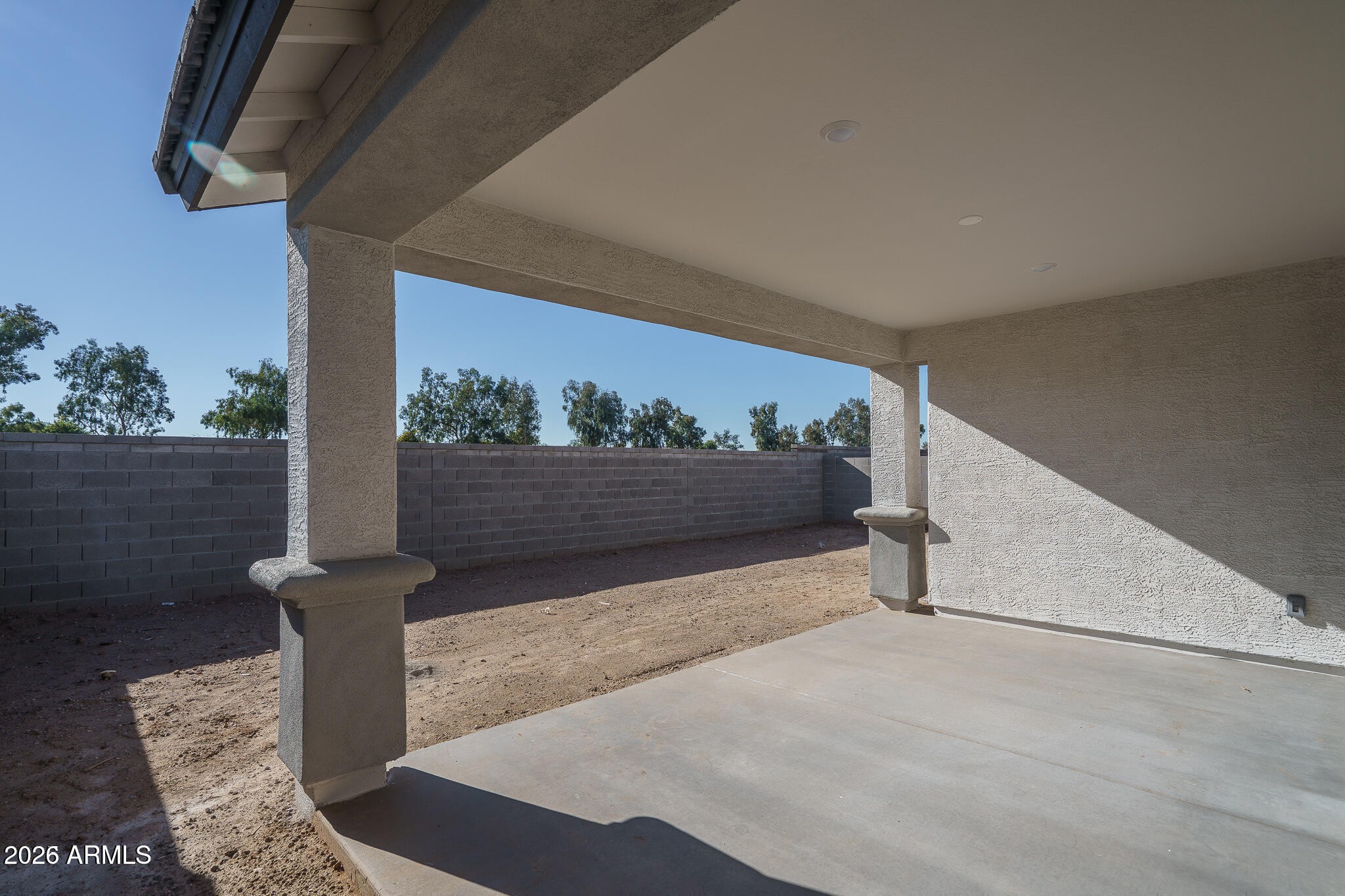Covered backyard patio with stucco columns, concrete flooring, and a walled dirt yard.