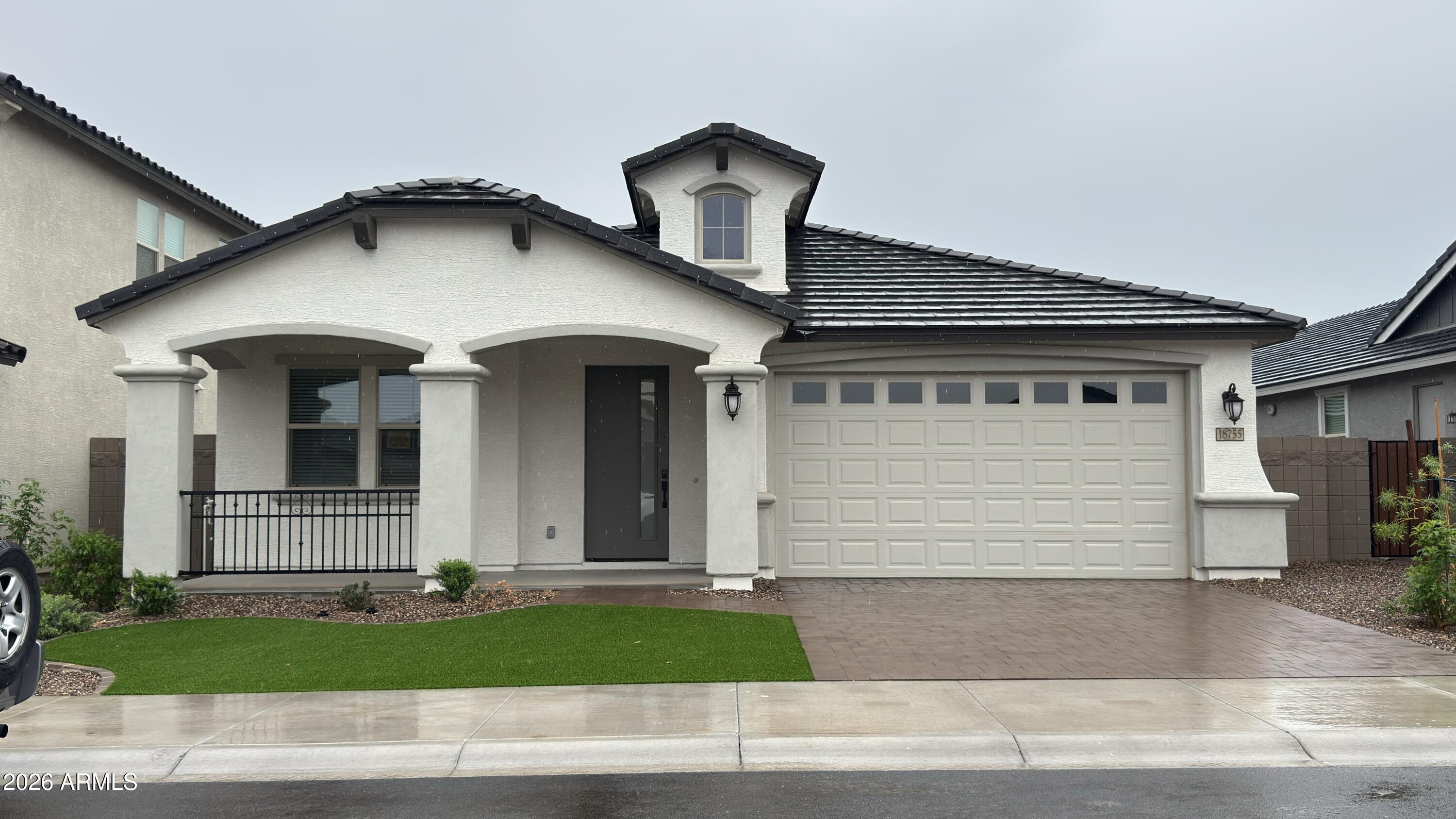 White stucco home with a dark tile roof, covered porch, and two-car garage.