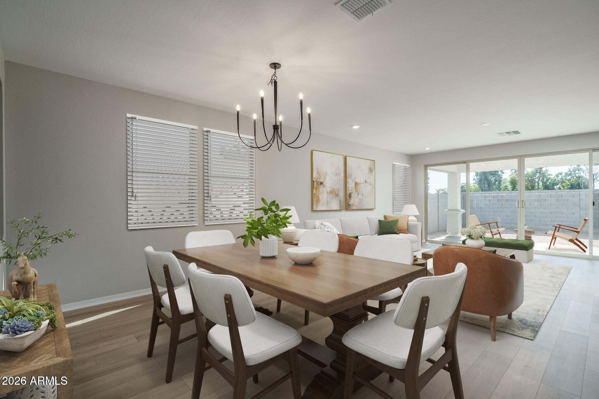 Dining area with a wood table and chandelier opens to a furnished living room and walled patio.