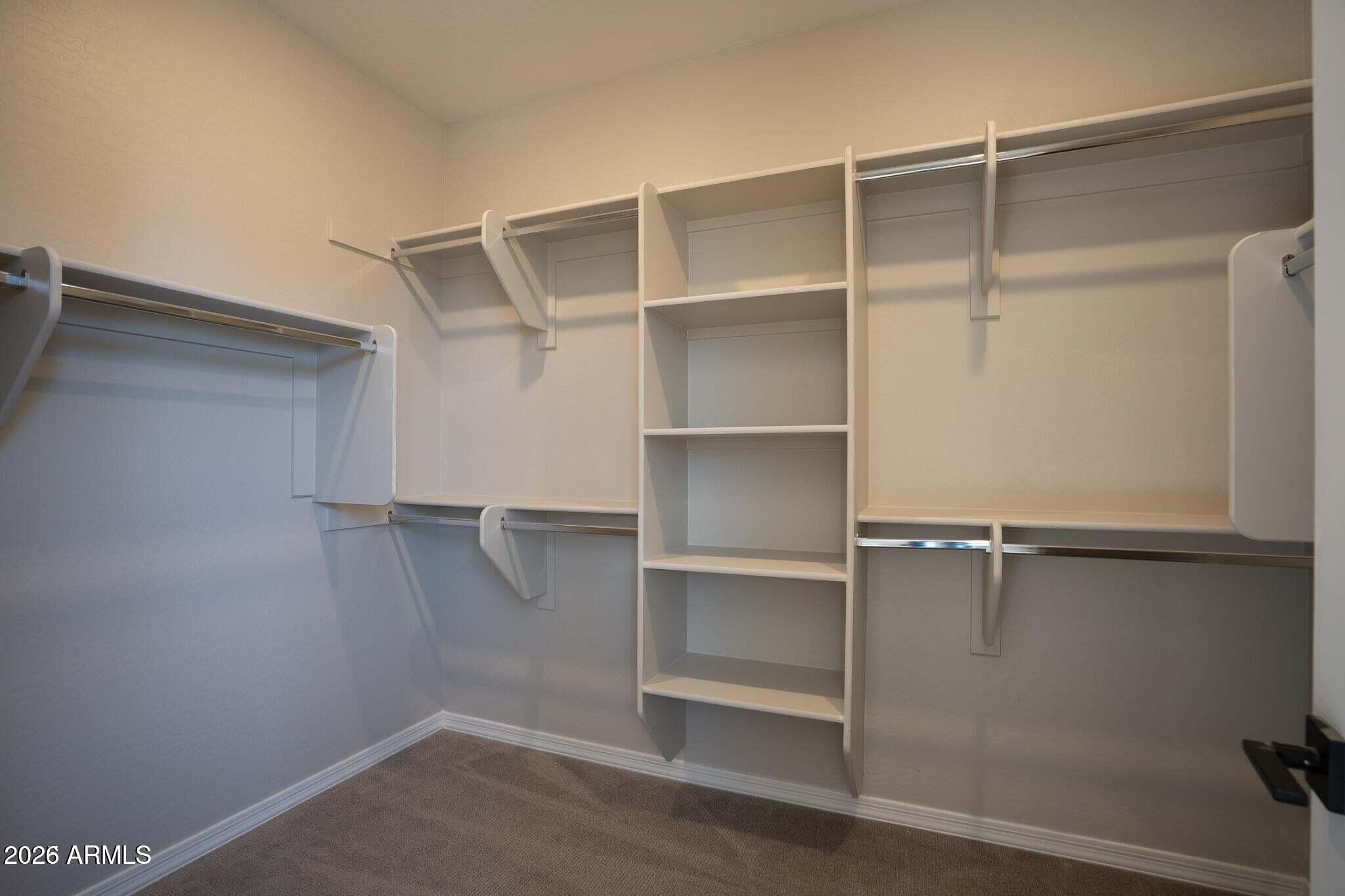 Empty walk-in closet with white built-in shelves and multiple hanging rods.