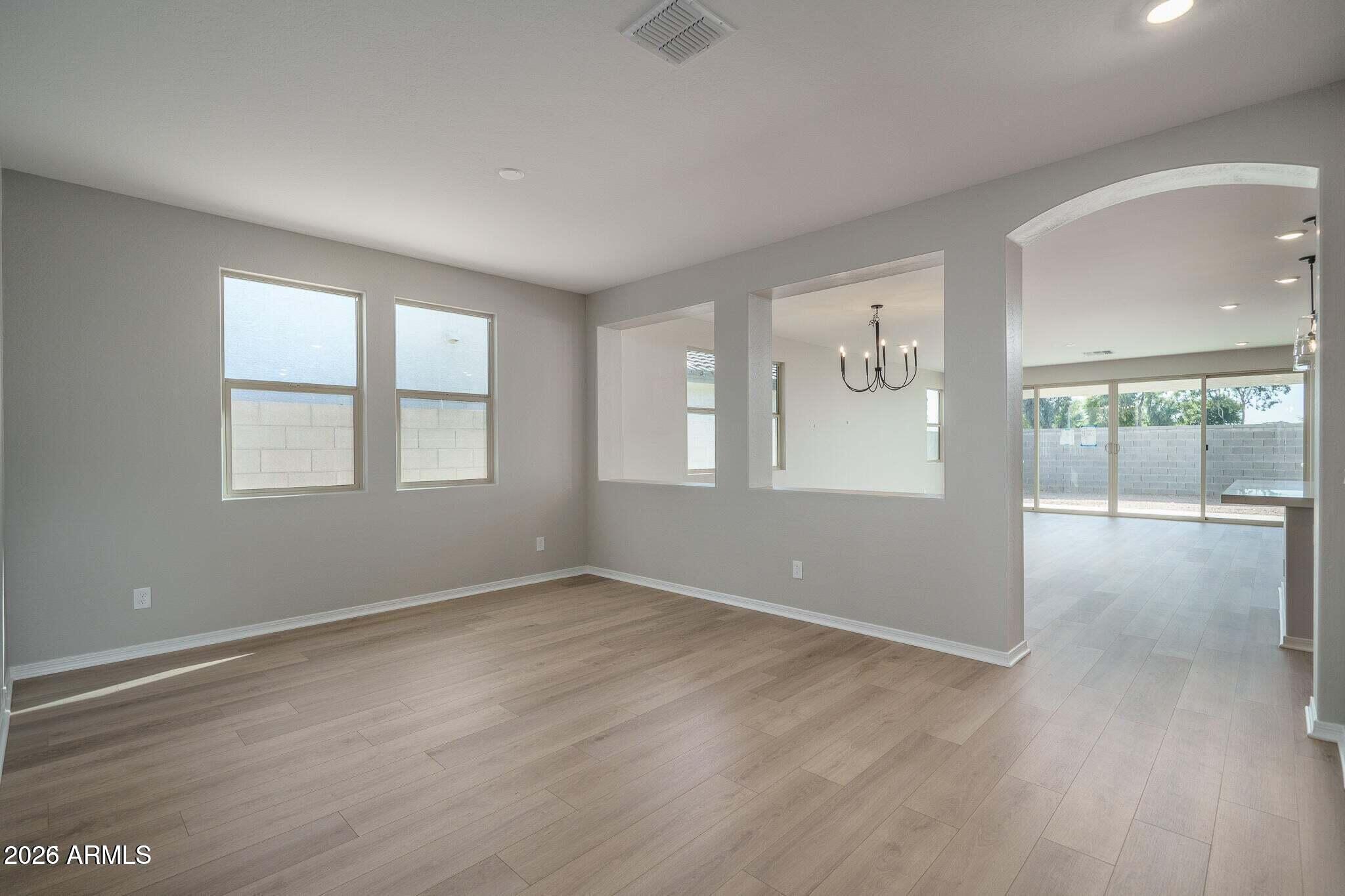 Empty dining area with plank flooring, two windows, and wide openings to a room with sliding glass doors.