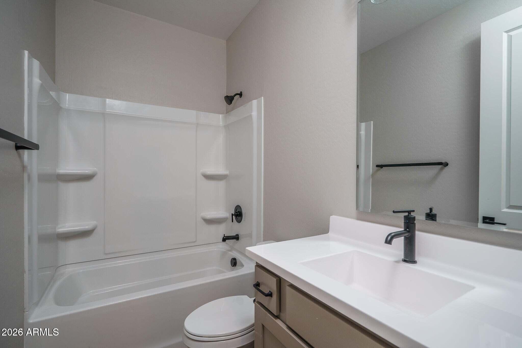 Bathroom with a white tub-shower, corner shelves, and a vanity with black fixtures.
