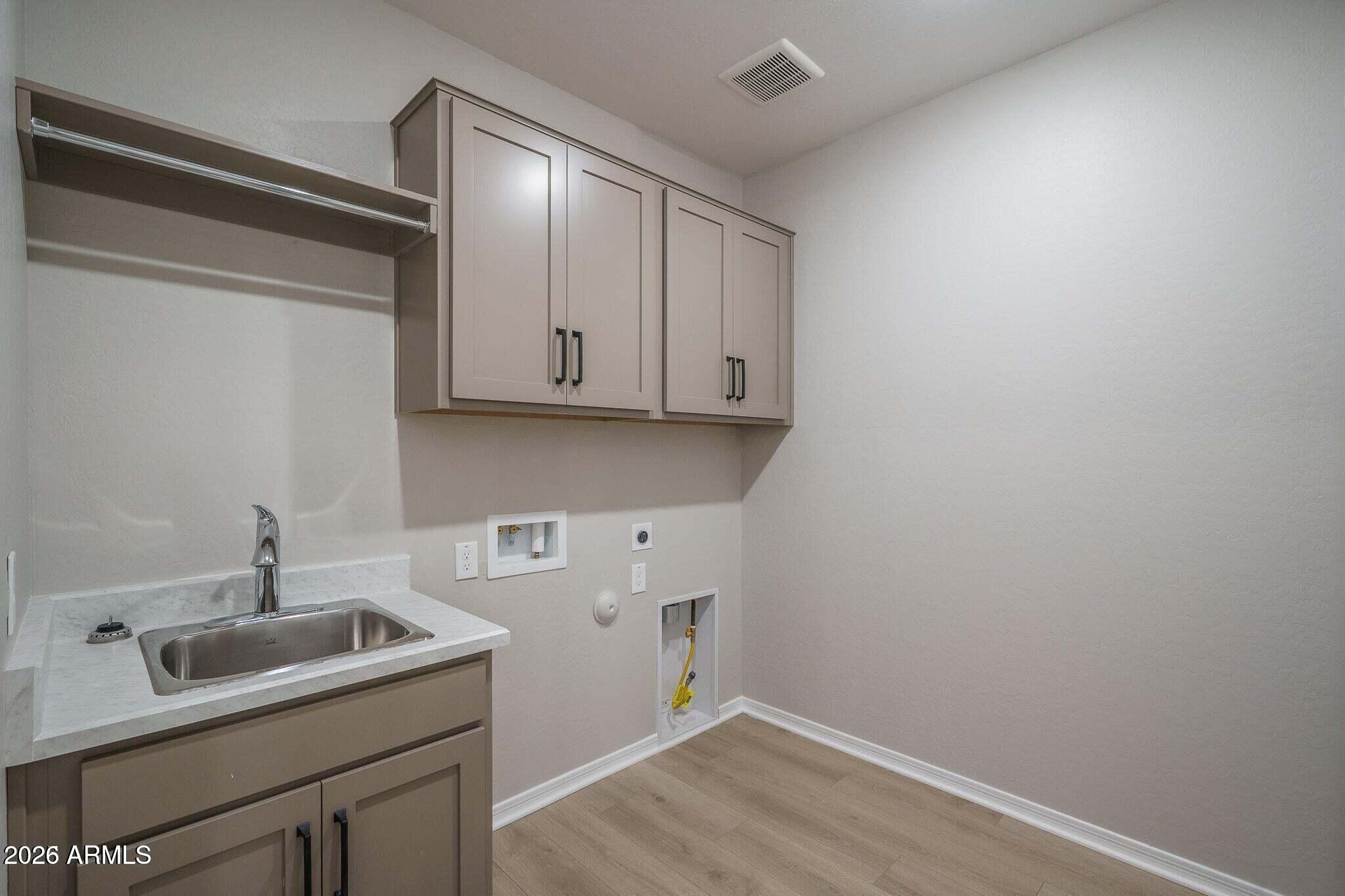 Laundry room with taupe cabinets, a utility sink, hanging rod, and washer hookups.