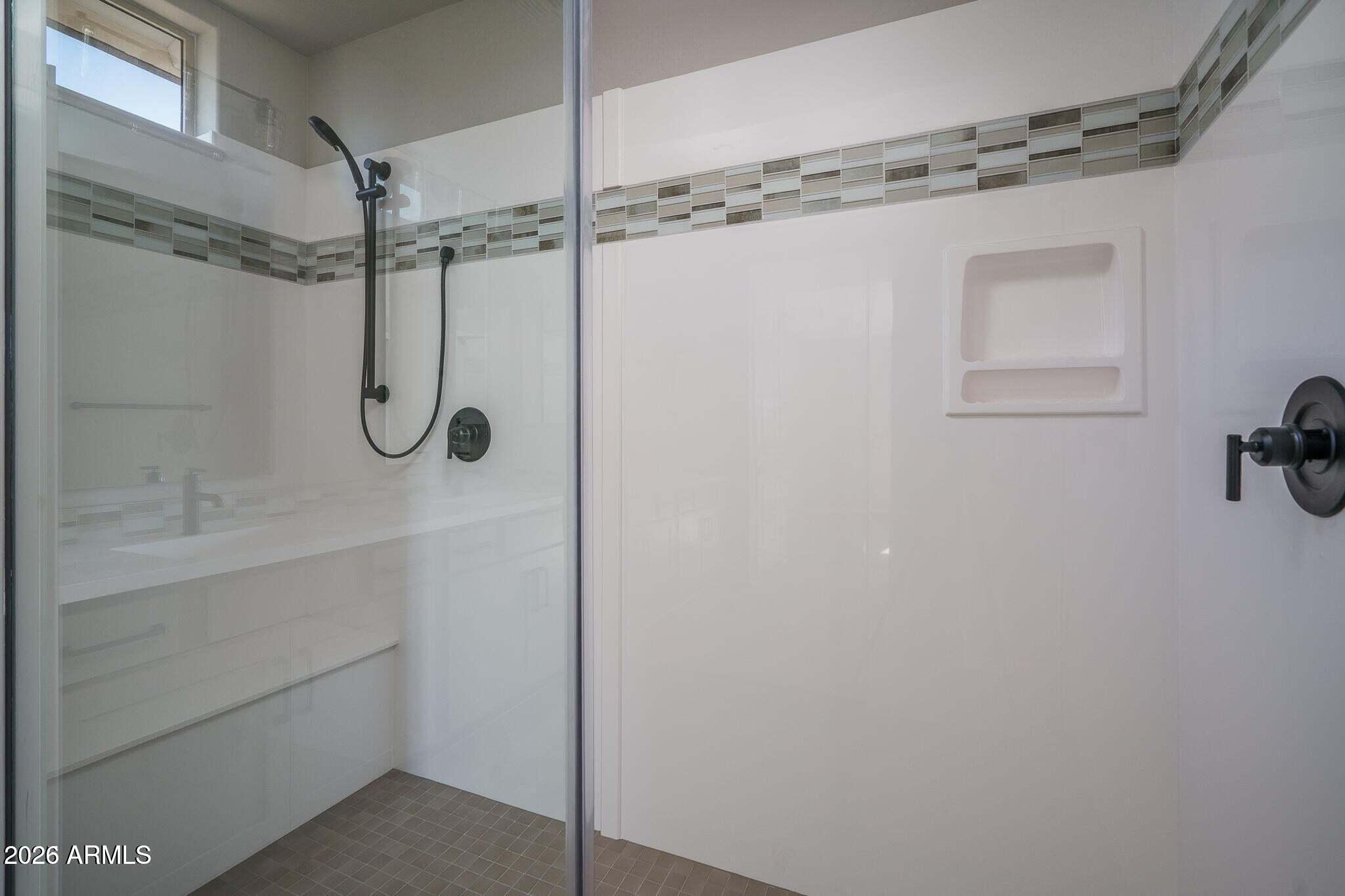 Glass-enclosed shower with black fixtures, built-in wall niche, and gray mosaic tile accent.