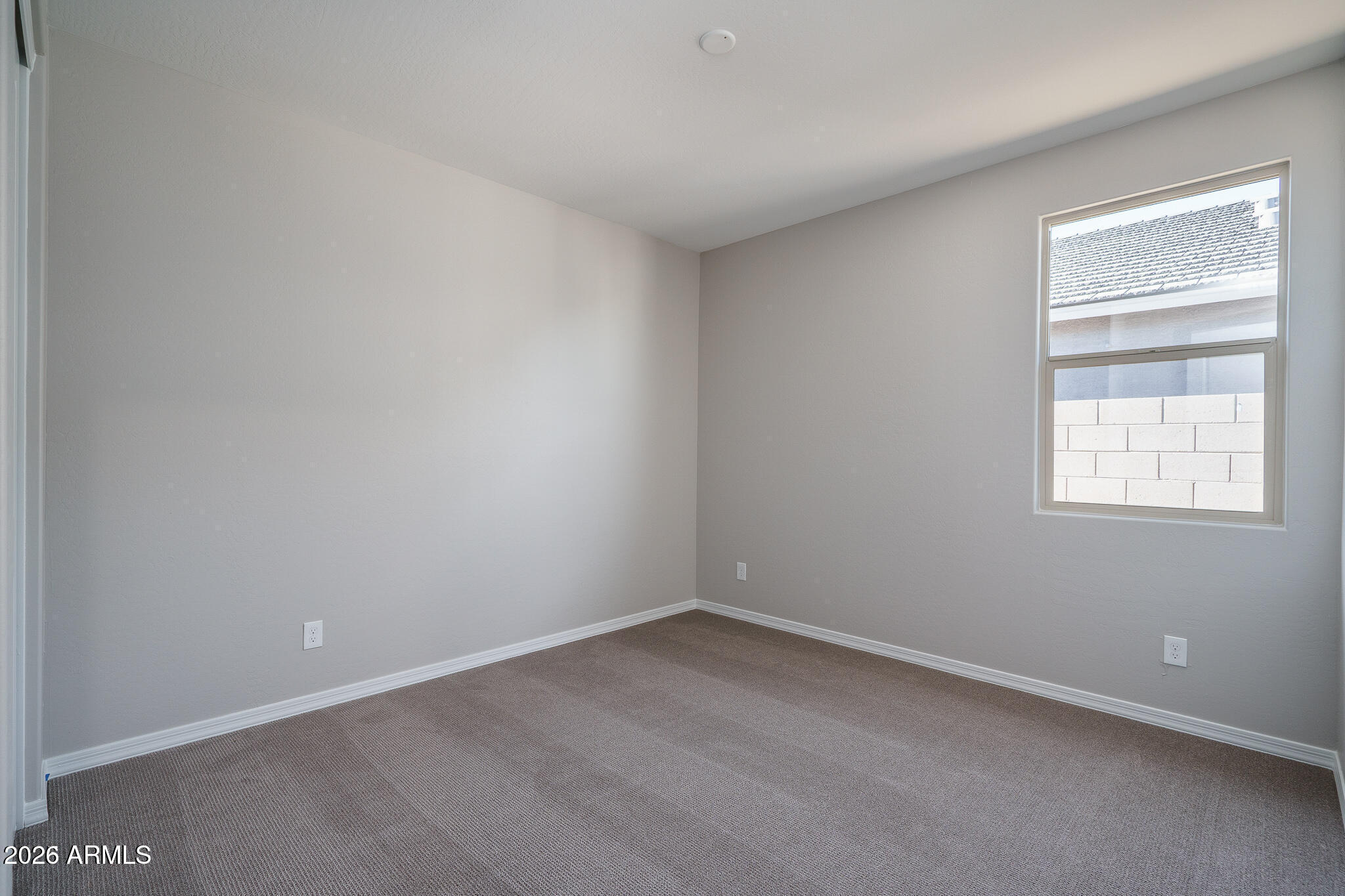 Empty bedroom with brown carpet, gray walls, and a window facing a block wall.