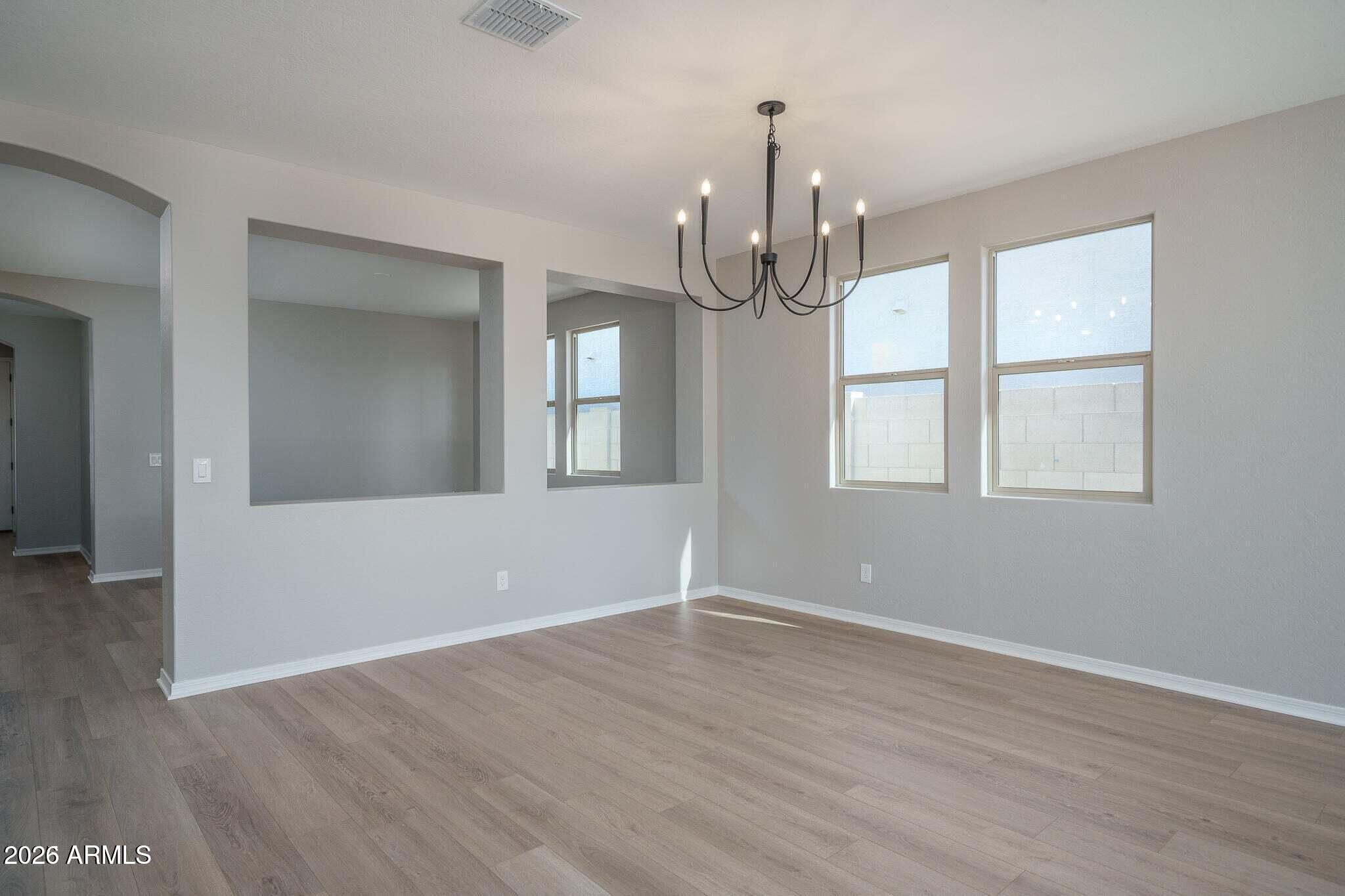 Empty dining room with wood-look floors, black chandelier, and wide openings to adjoining rooms.