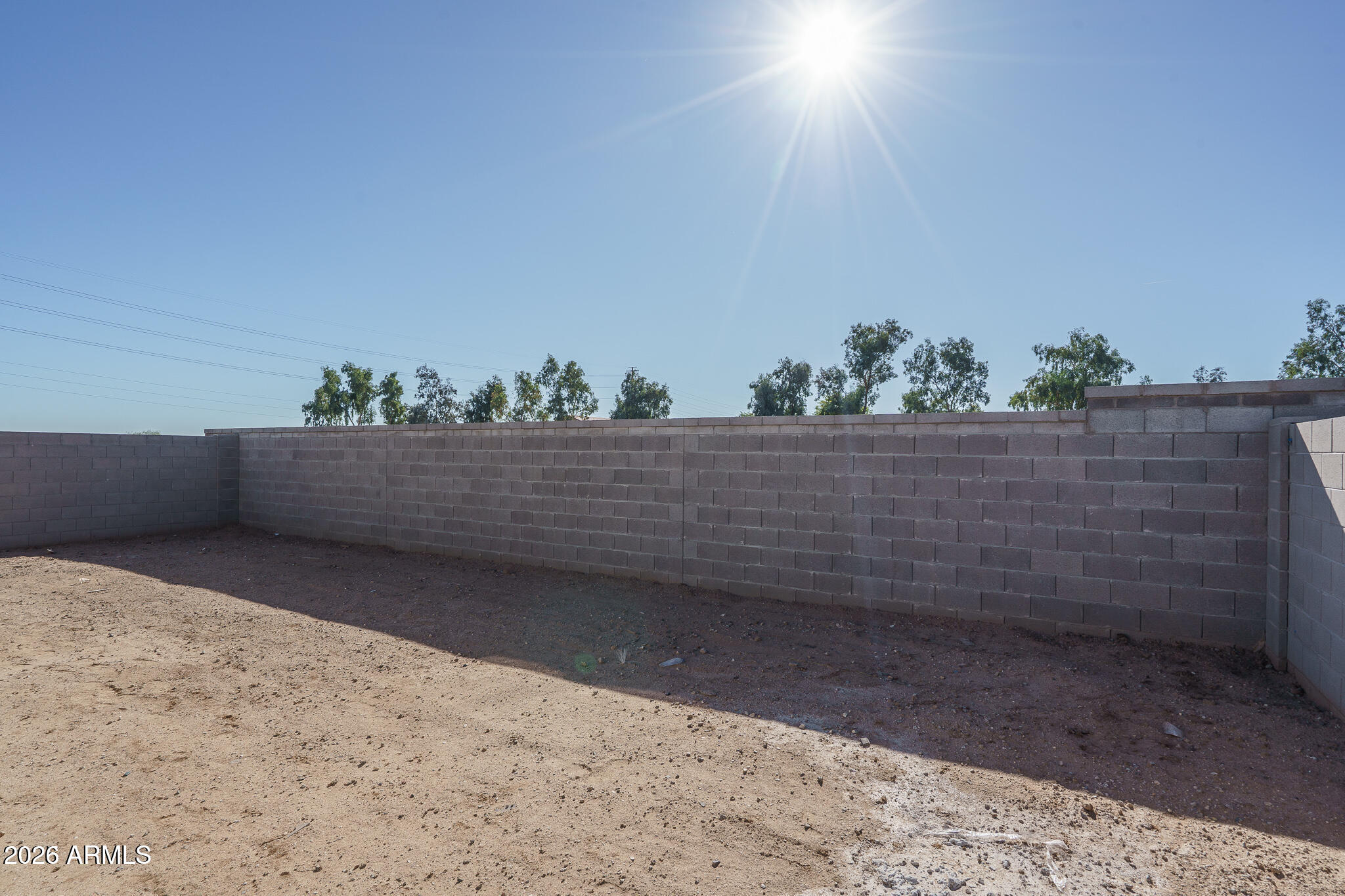 Bare dirt backyard enclosed by a tall block wall under bright sun.
