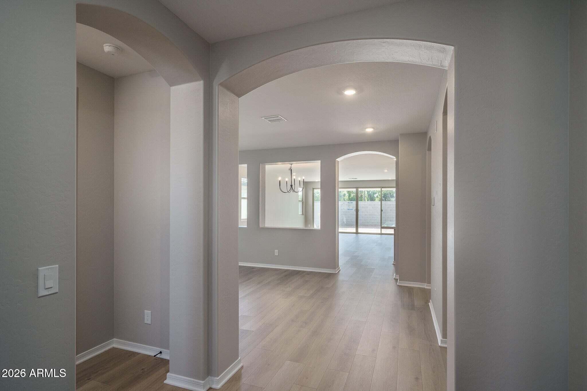 Empty home interior with arched hallways, light wood-look floors, a black chandelier, and sliding glass doors.