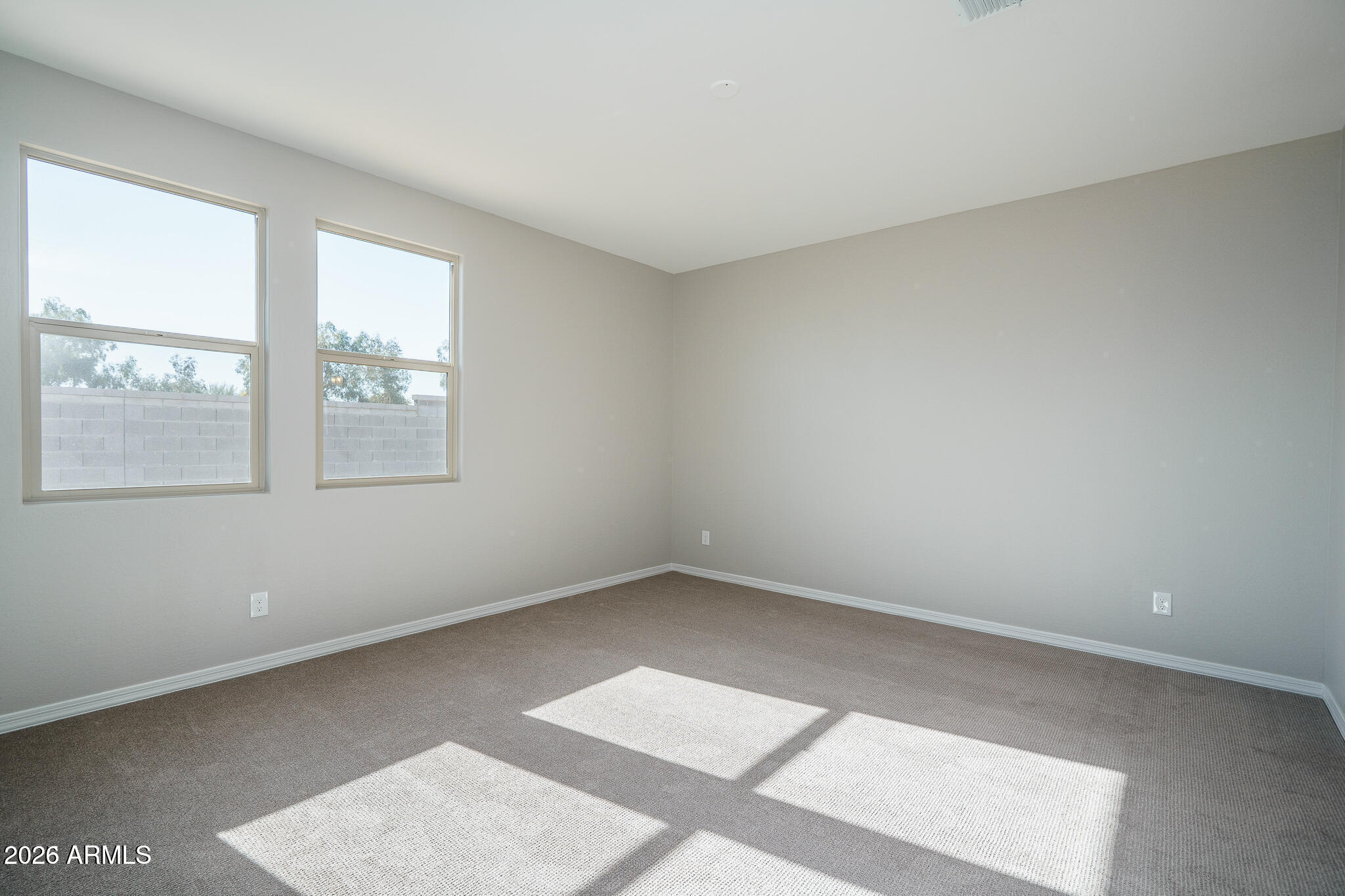 Empty carpeted room with two windows and sunlight streaming across the floor.