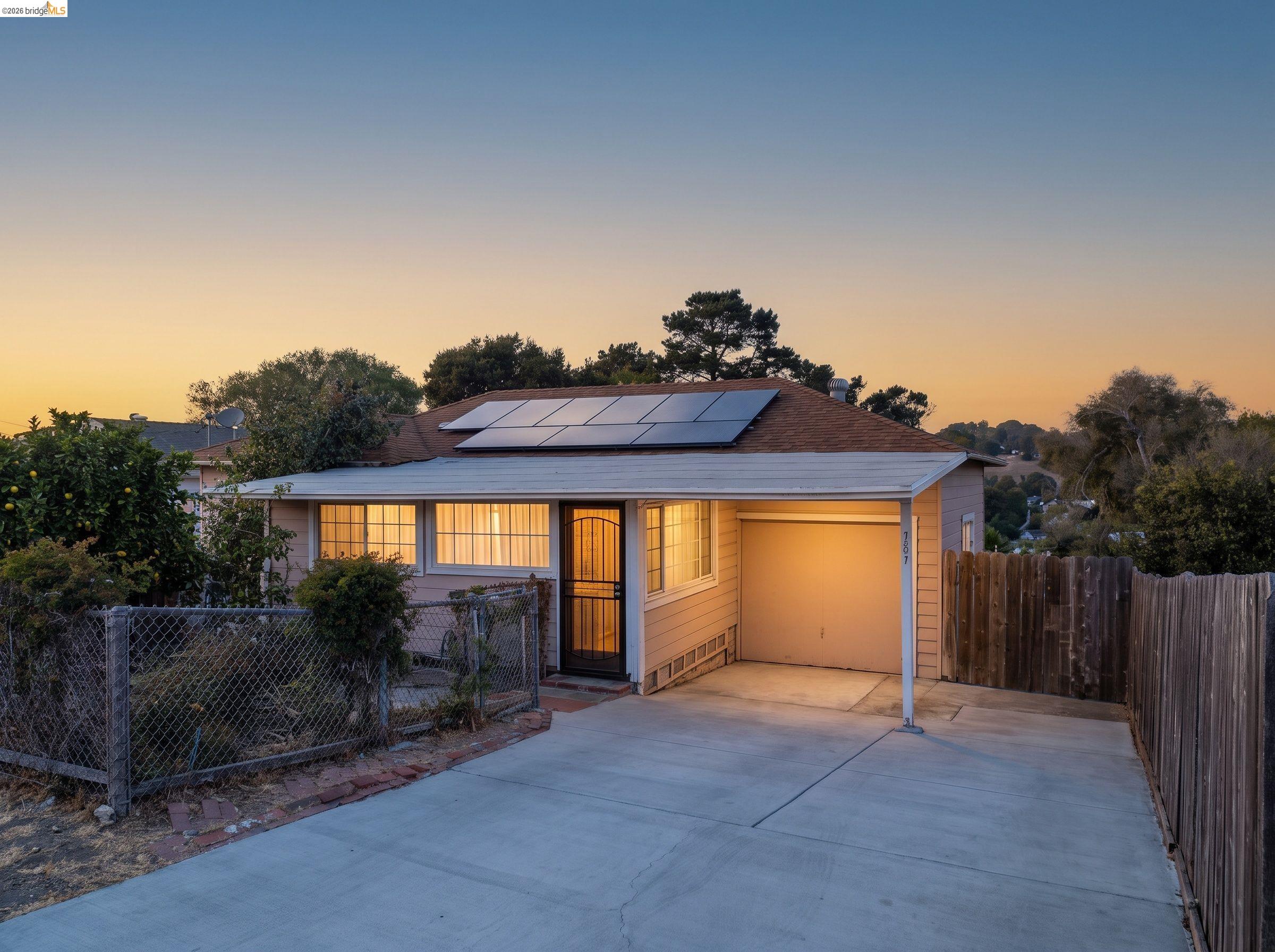 Single-story home at dusk with rooftop solar panels, a warmly lit entry, and a wide driveway.