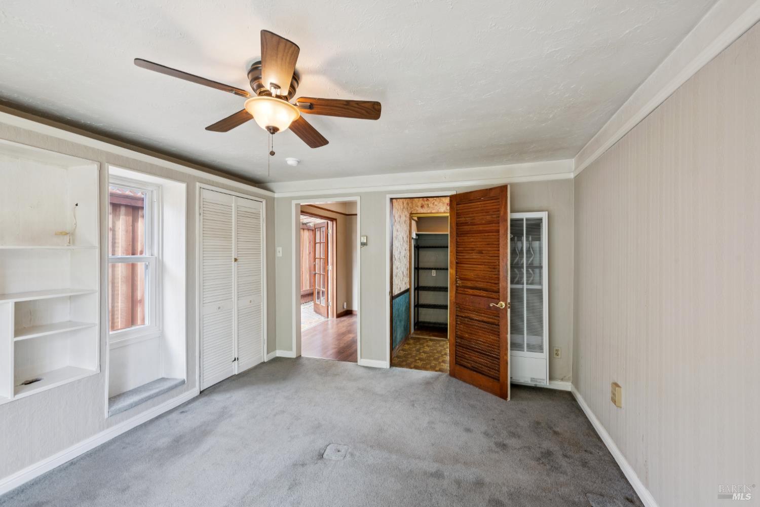 Empty carpeted room with a ceiling fan, built-in shelves, and an open closet.
