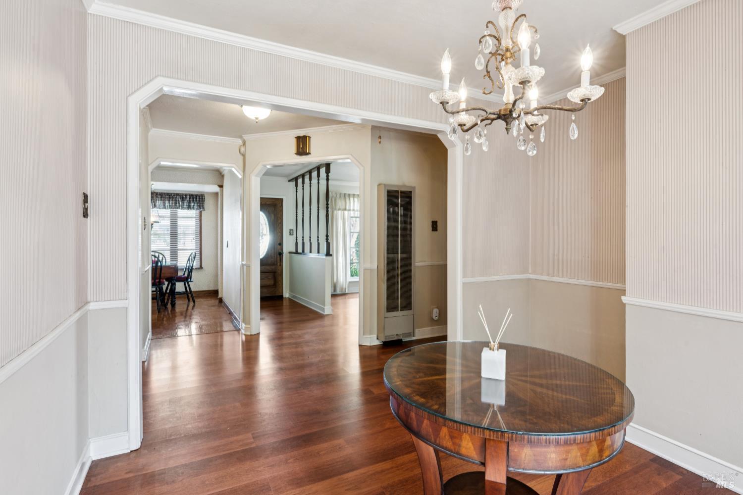 Furnished dining room with a round wood table, crystal chandelier, and hardwood floors.