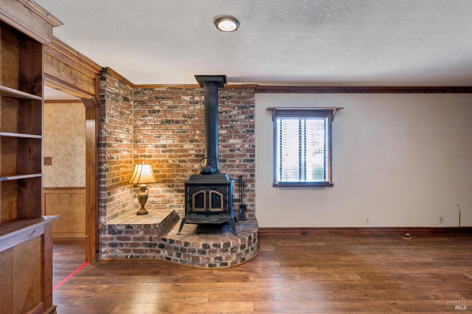 Living room with a freestanding wood stove against a brick fireplace surround and built-in wooden shelving.
