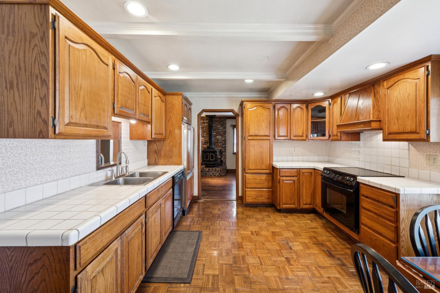 Kitchen with honey-toned wood cabinets, white tile counters, and parquet flooring.