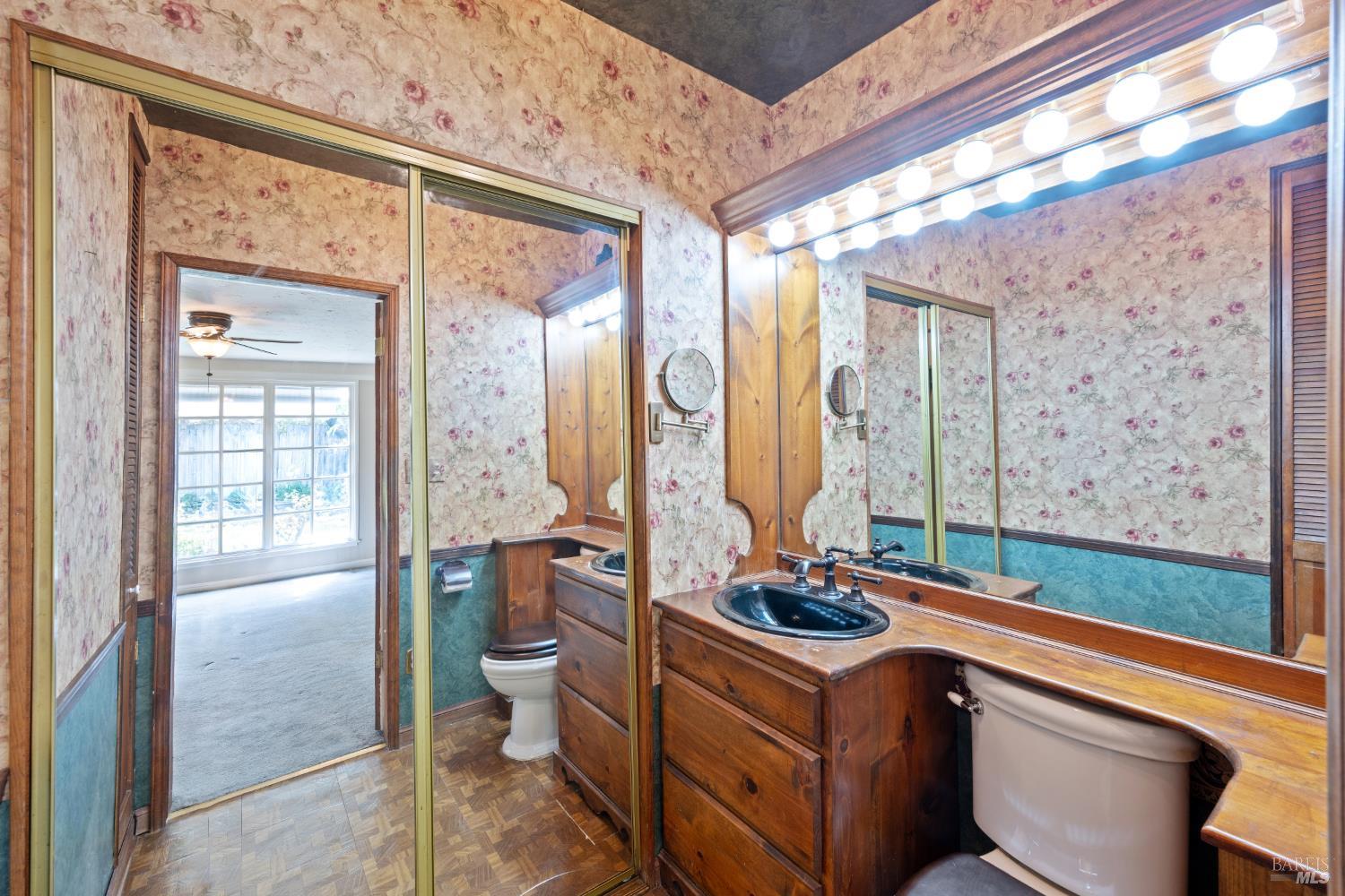 Bathroom with a double-sink wood vanity, mirrored cabinets, and floral wallpaper.