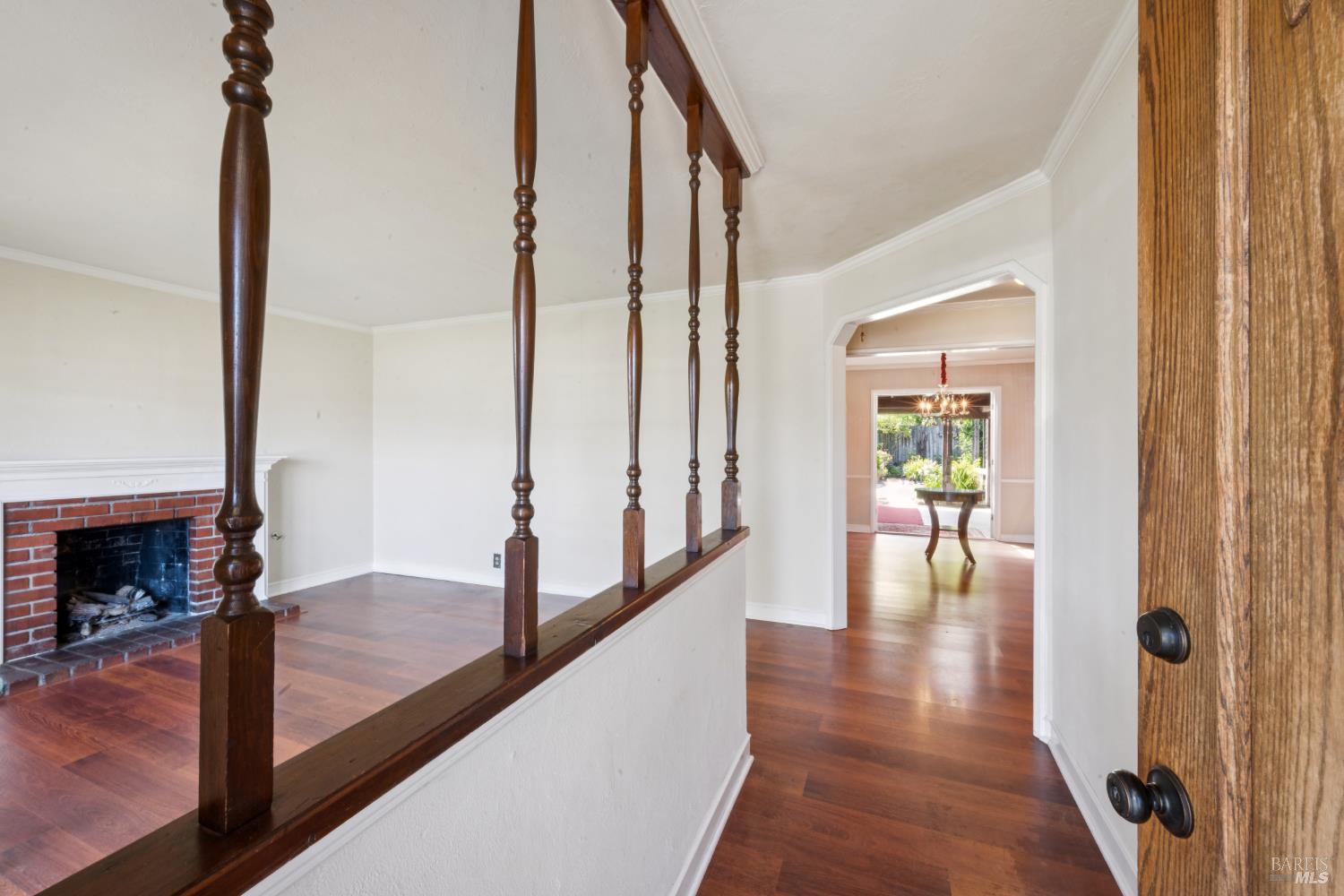 Interior hallway with dark wood railing, brick fireplace, and view into a dining room.