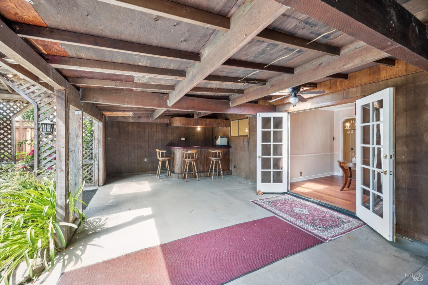 Covered patio with exposed wooden beams, a small bar, and open French doors.