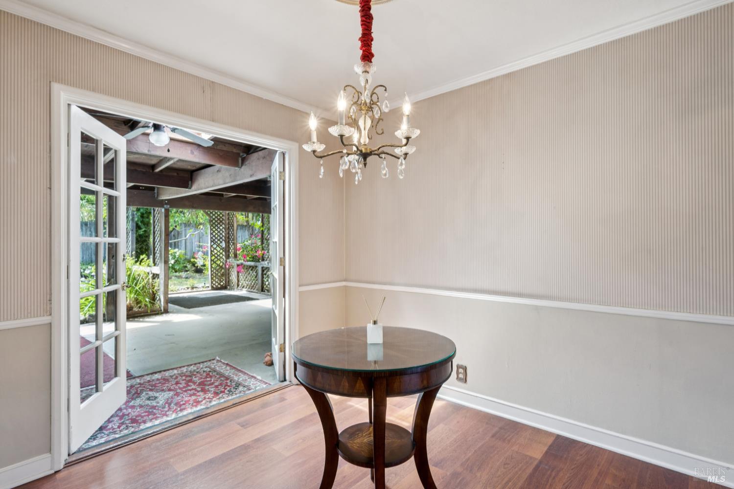 Dining room with a round wooden table and chandelier; open French doors lead to a covered patio.