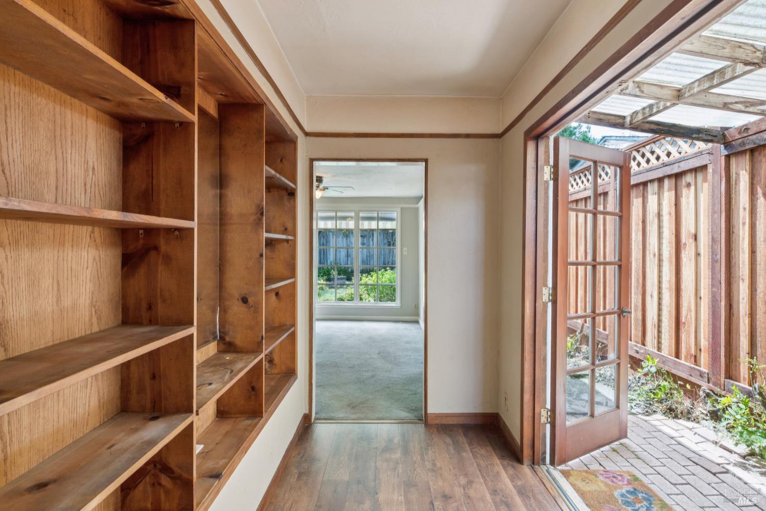 Hallway with built-in wood shelving and an open glass door to a covered patio.