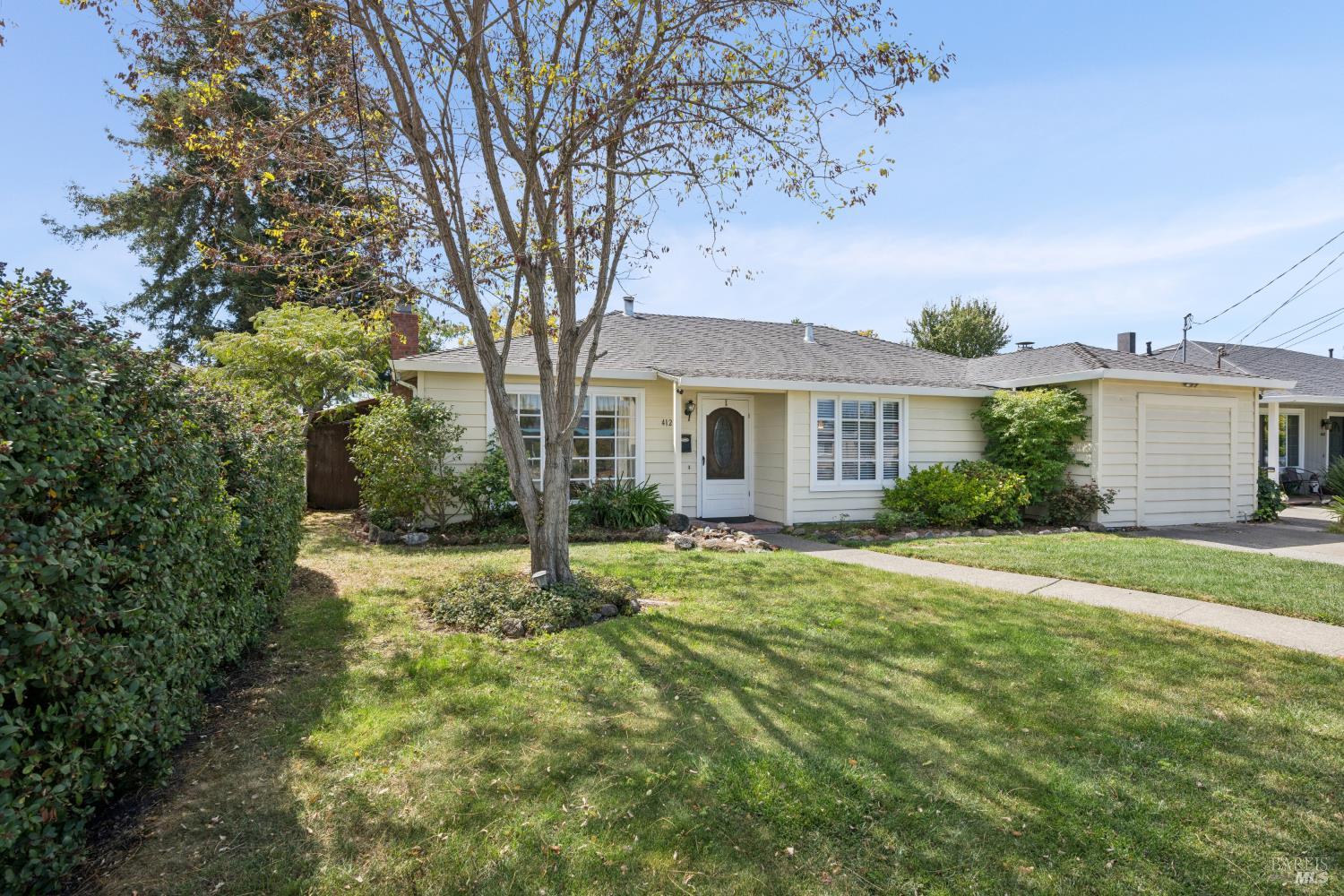 Single-story home with an attached garage, mature front-yard tree, and landscaped lawn.