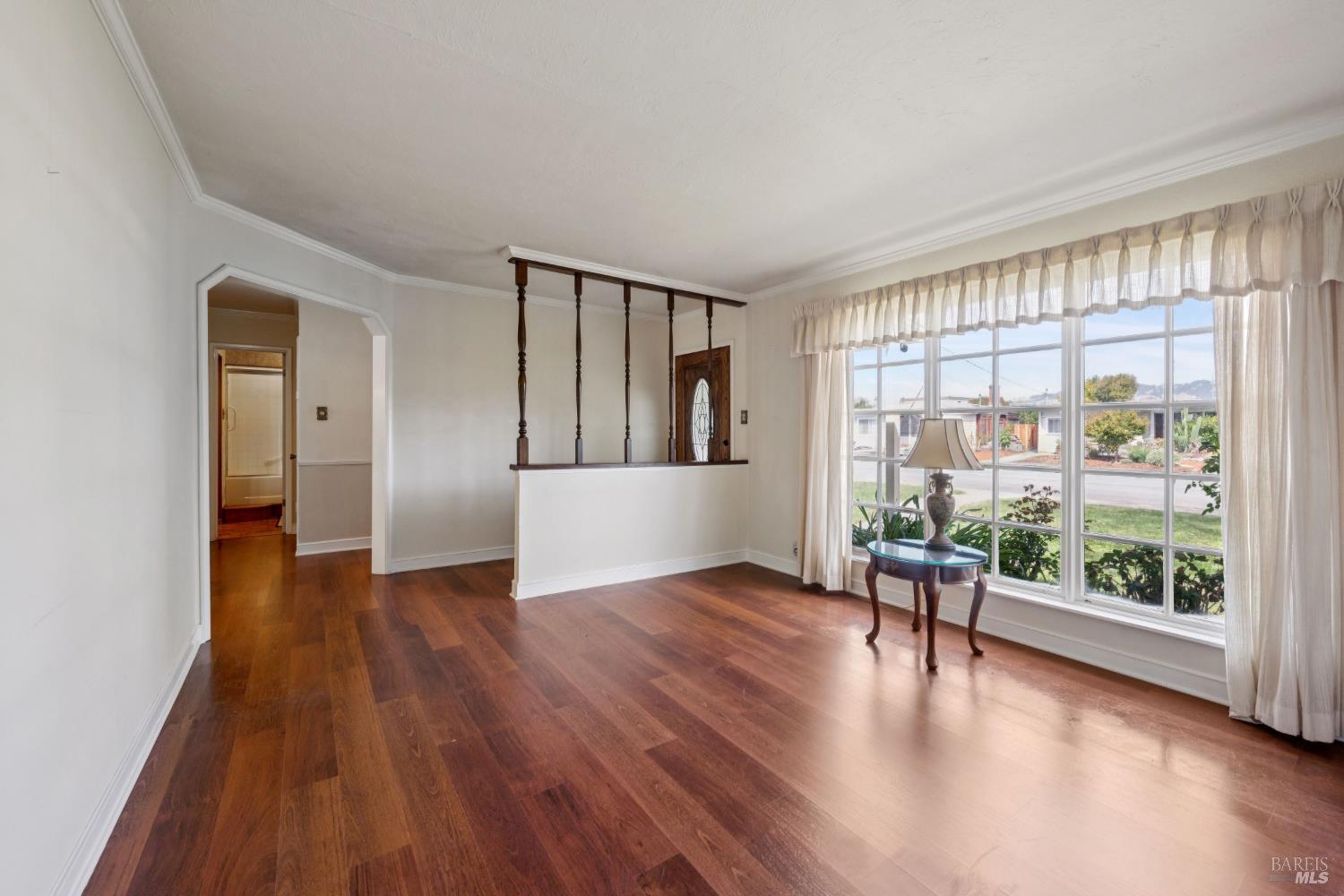 Living room with polished hardwood floors, a large curtained window, and a half-height partition with wood spindles.