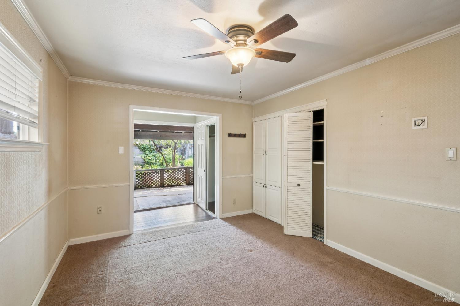 Empty bedroom with beige carpet, built-in closets, and an open doorway to a garden patio.