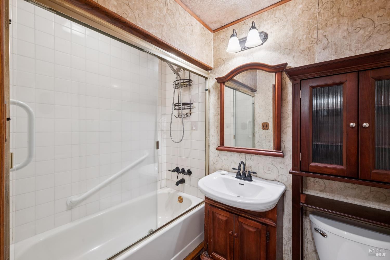 Bathroom with a tiled tub-shower, dark wood vanity, framed mirror, and matching storage cabinet.