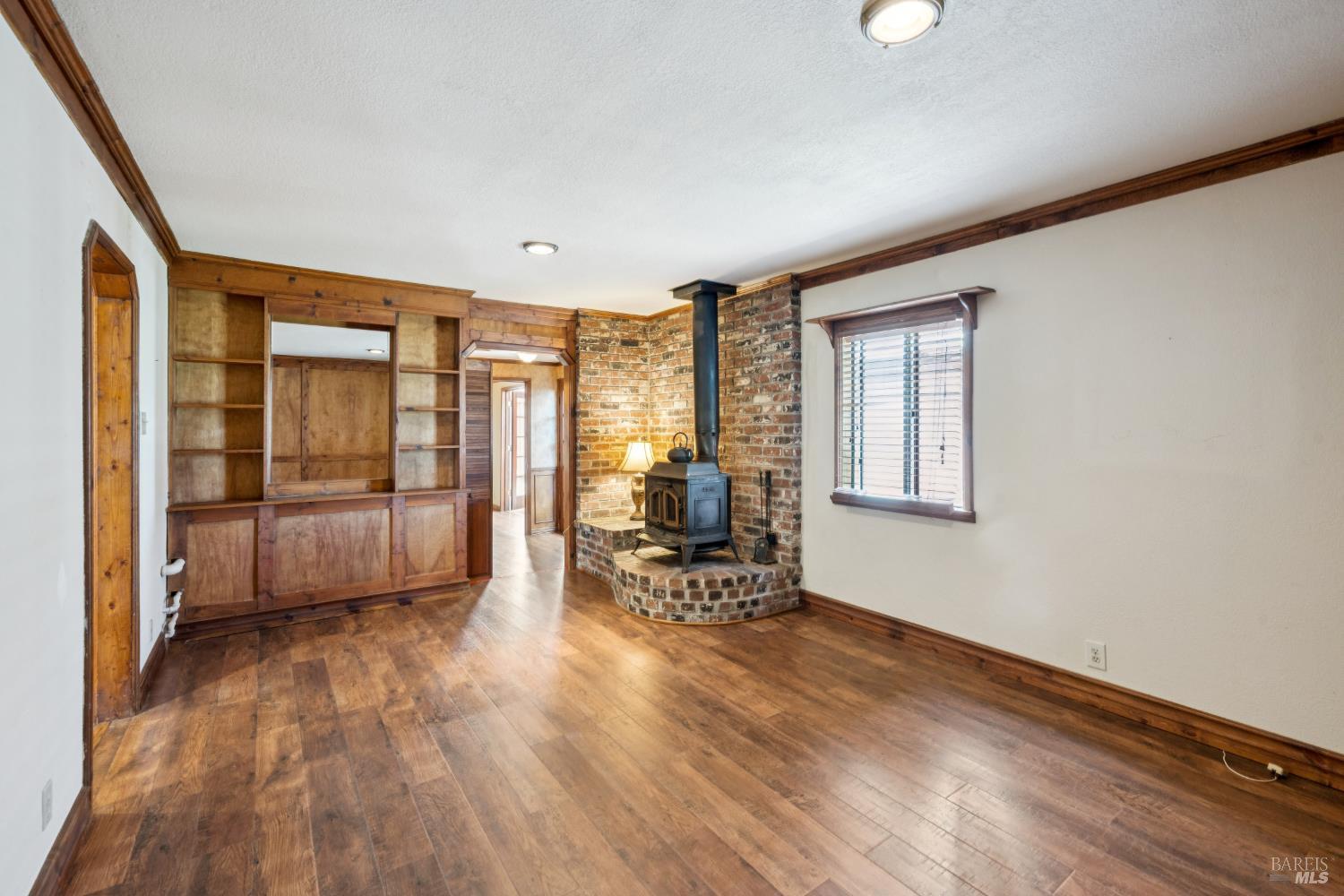Room with hardwood floors, built-in wood shelving, and a black stove on a brick hearth.