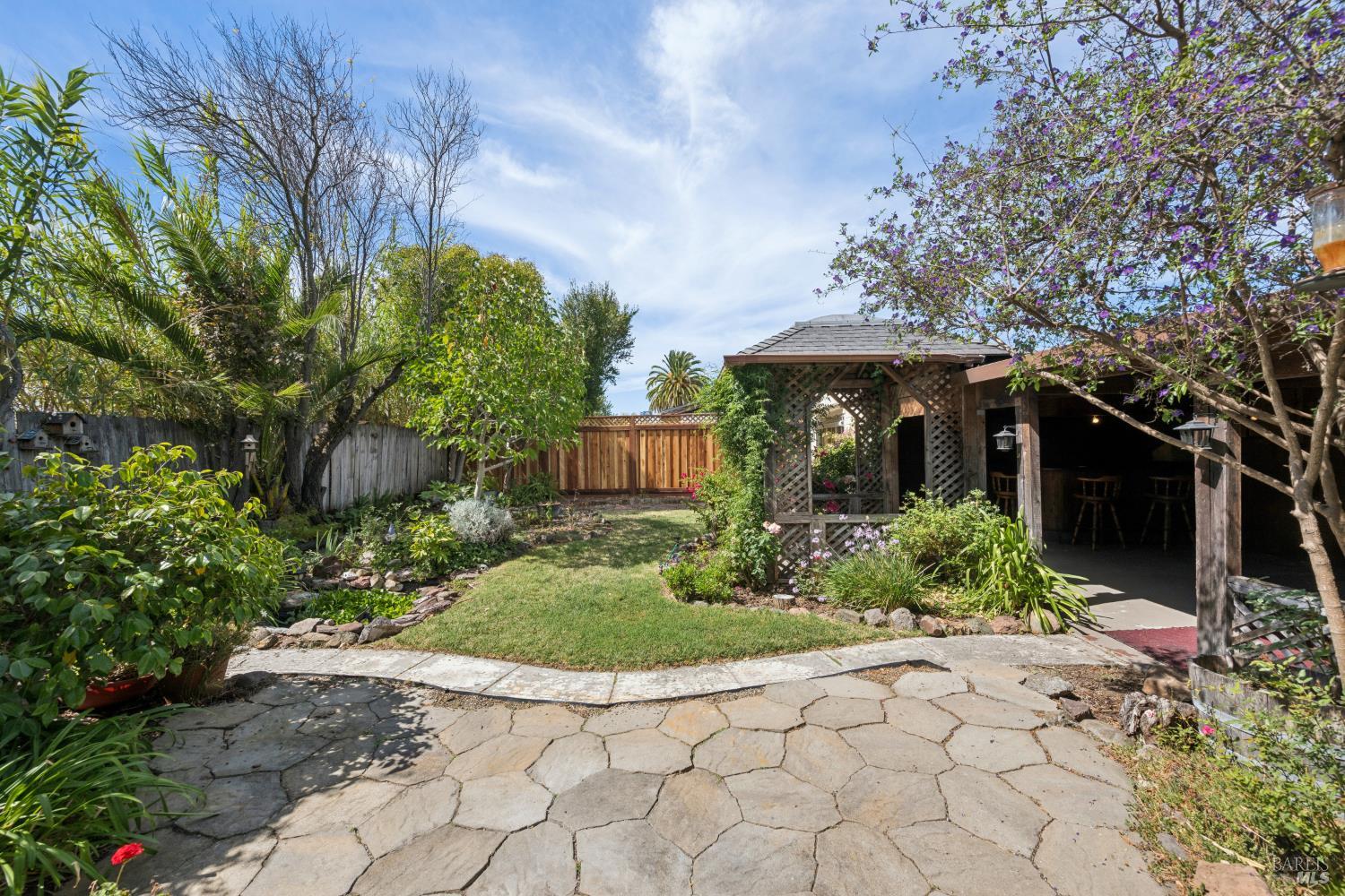 Backyard patio with stone paving, landscaped garden, and a shaded wooden pergola.