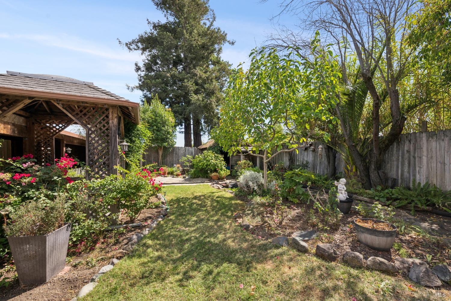 Landscaped backyard with a wooden pergola, flowering shrubs, and a small lawn.