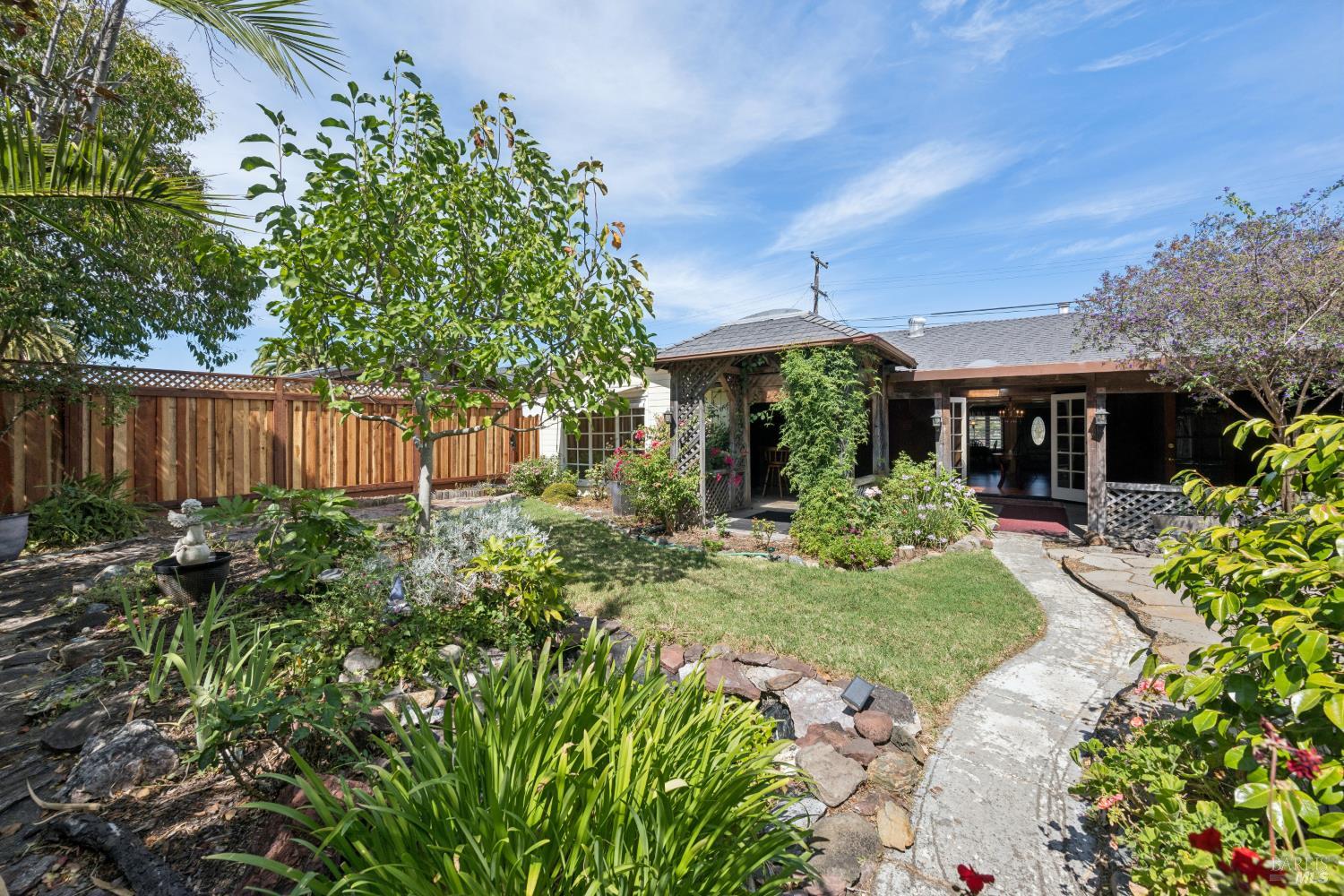 Landscaped backyard with a covered patio, wooden fence, and winding stone walkway.