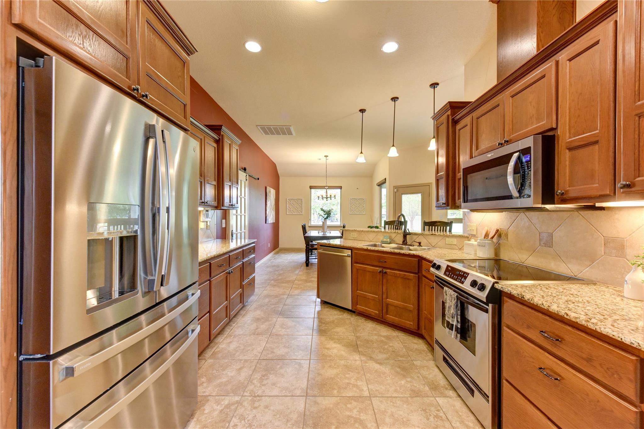 Kitchen with wood cabinets, stainless steel appliances, tiled floors, and a dining area by the windows.