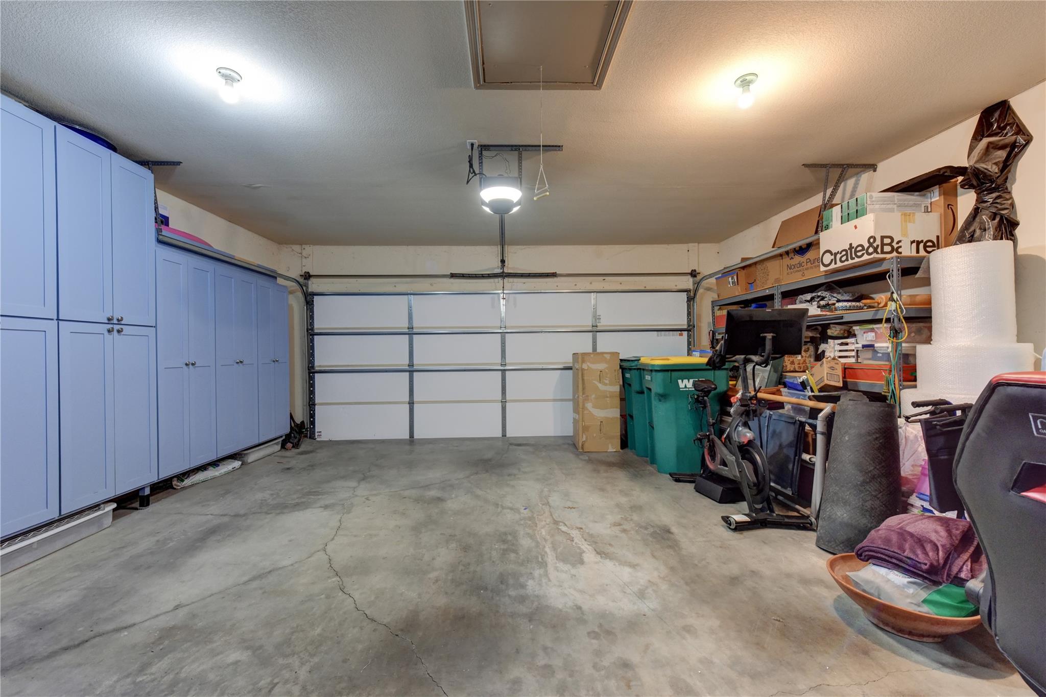 Garage with blue storage cabinets, a closed garage door, and shelving crowded with boxes and equipment.