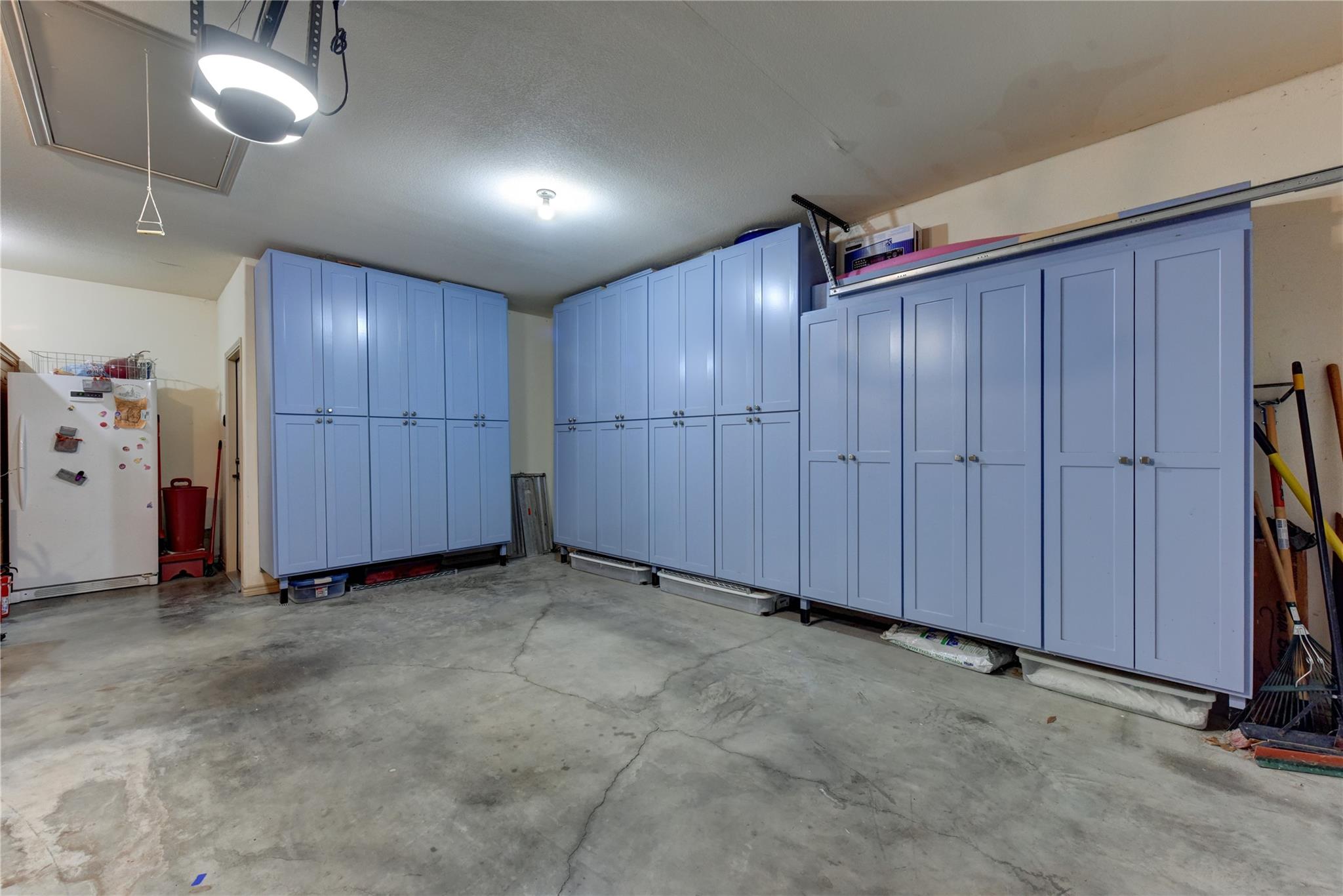 Garage with blue storage cabinets lining two walls and a cracked concrete floor.