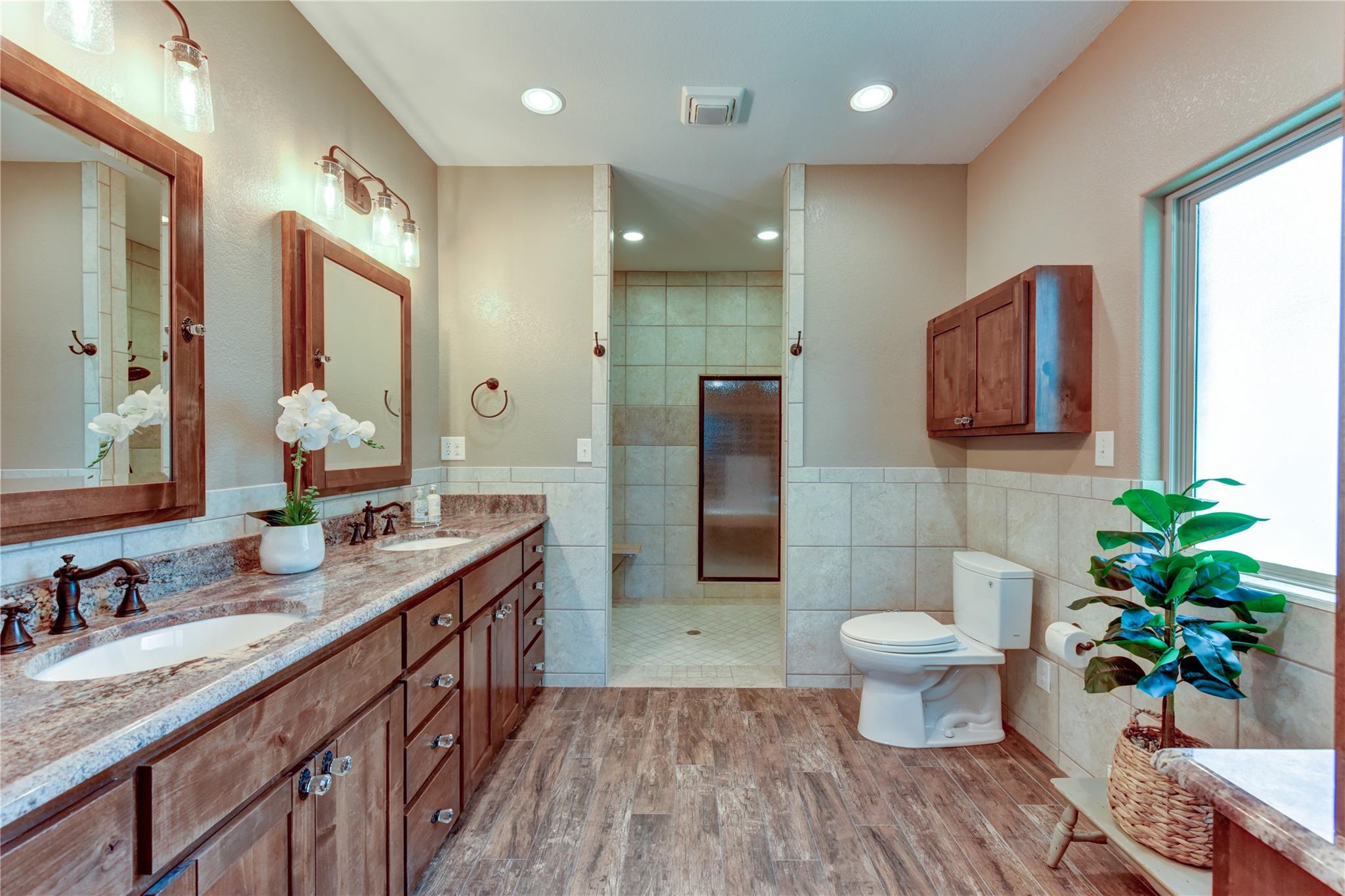Bathroom with a long double-sink vanity, tiled walk-in shower, and large window.