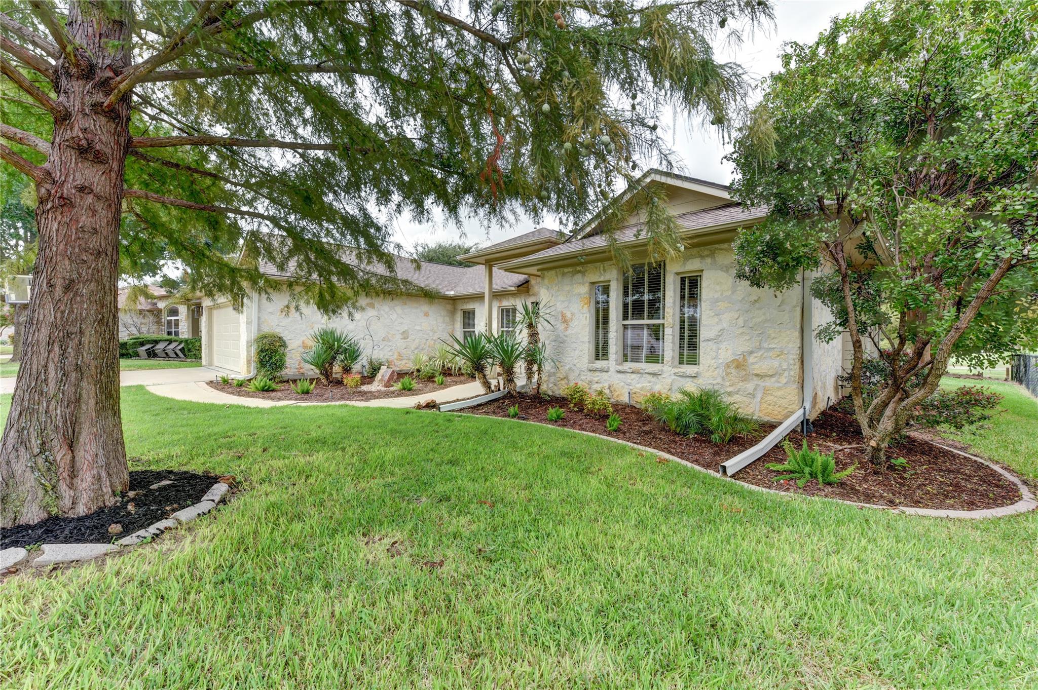 Stone-front home with an attached garage, landscaped beds, broad lawn, and mature trees.