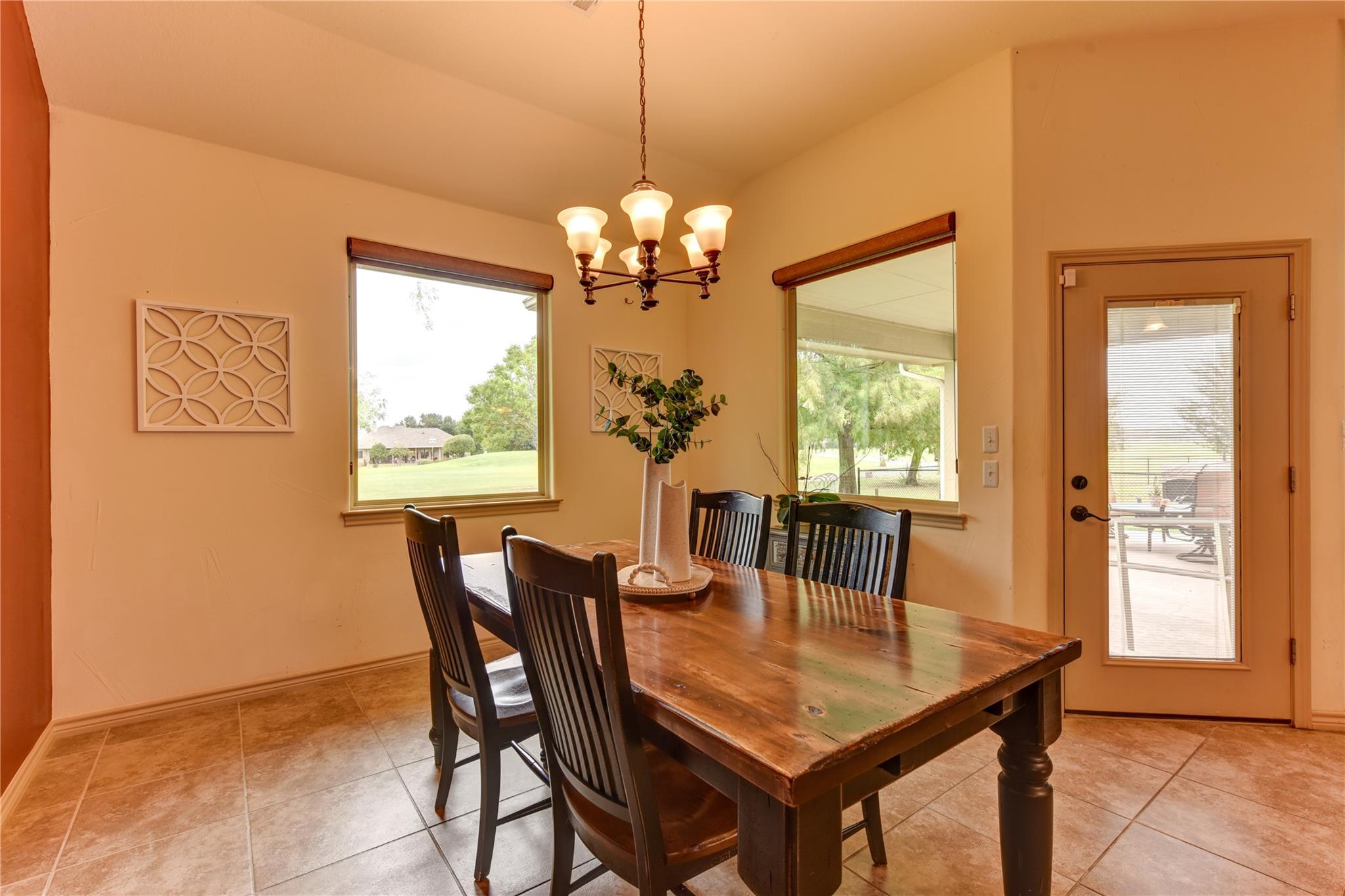 Furnished dining room with a rustic wood table, chandelier, and windows overlooking a green lawn.