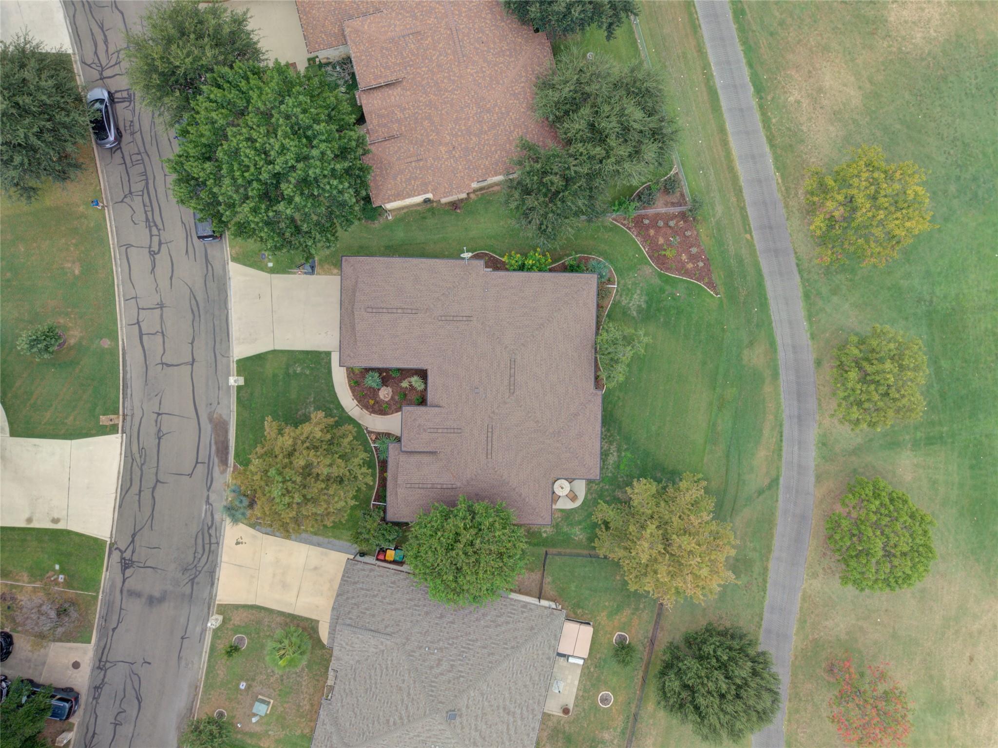 Aerial view of a brown-roofed home with landscaped lawn and curved front walkway.