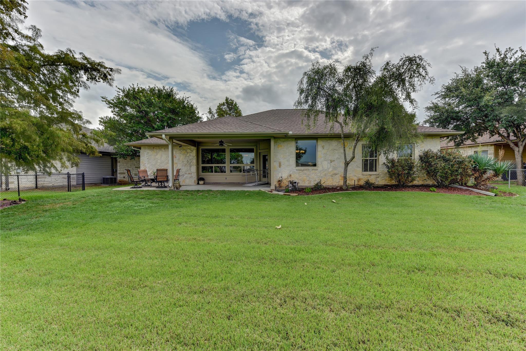 Single-story stone home with a covered patio and seating behind a broad green lawn.