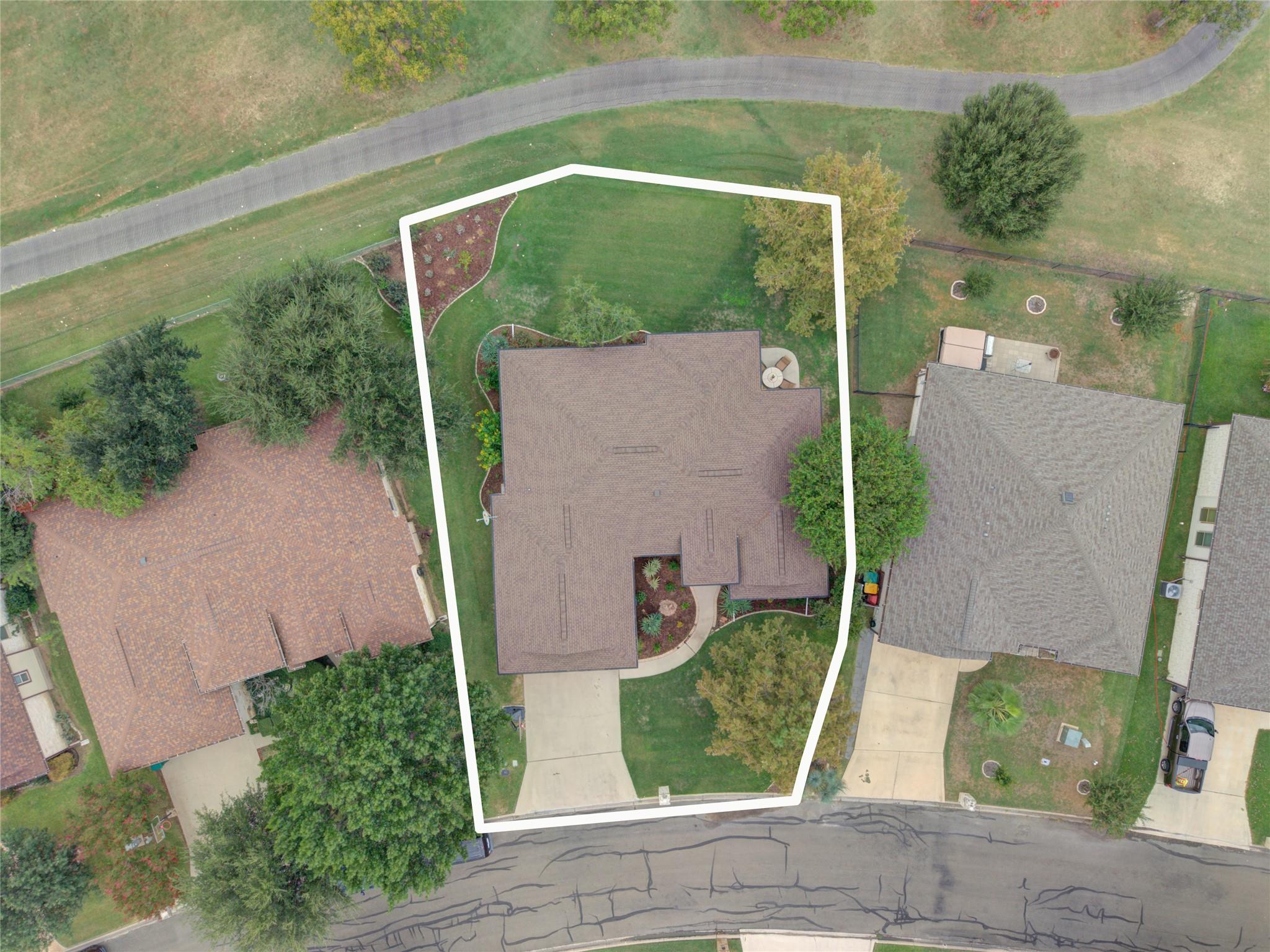Aerial view of a house and landscaped lot outlined in white, with a driveway and mature trees.