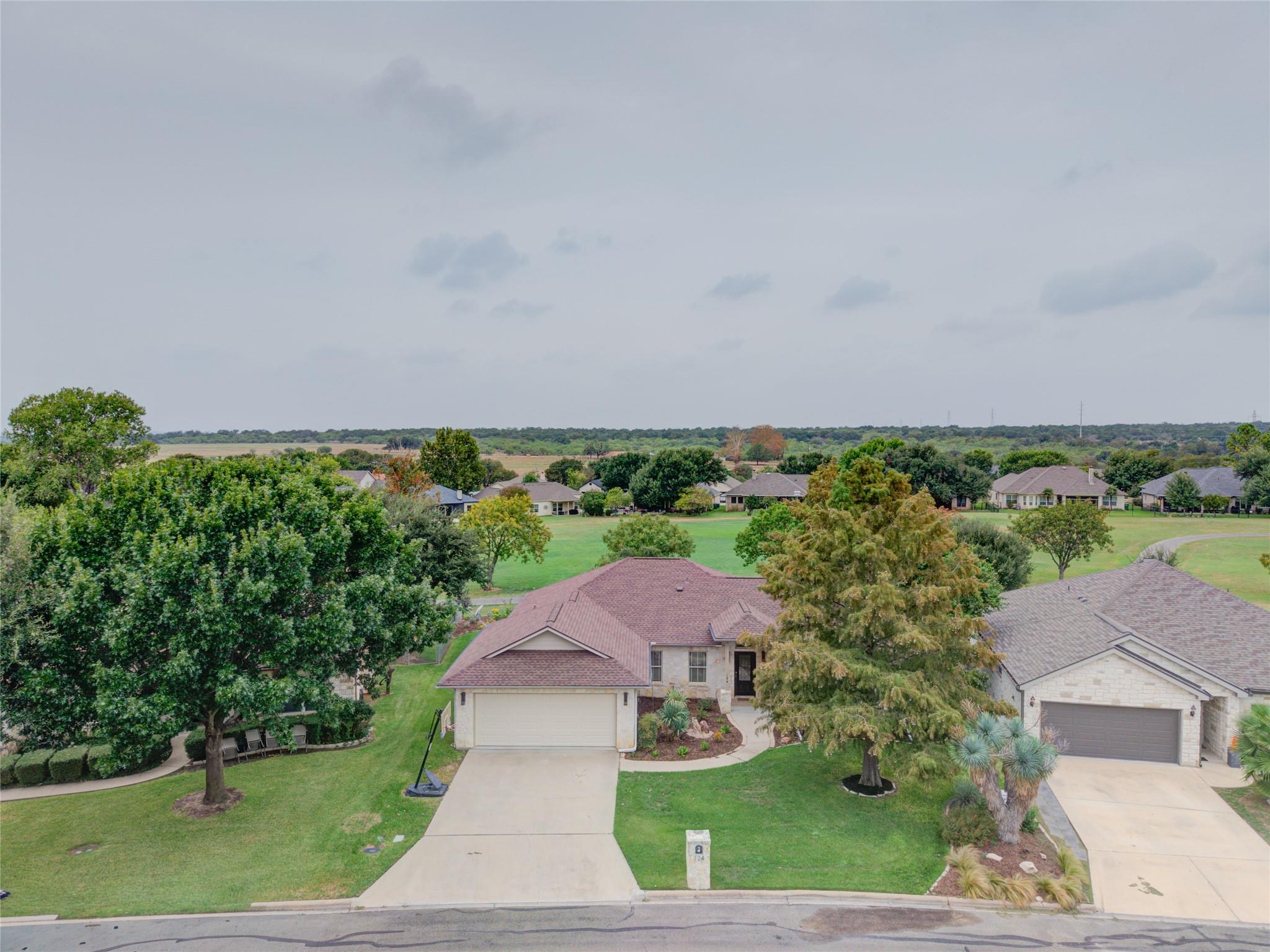 Aerial view of a stone-front home with a curved walkway, landscaped yard, and basketball hoop.