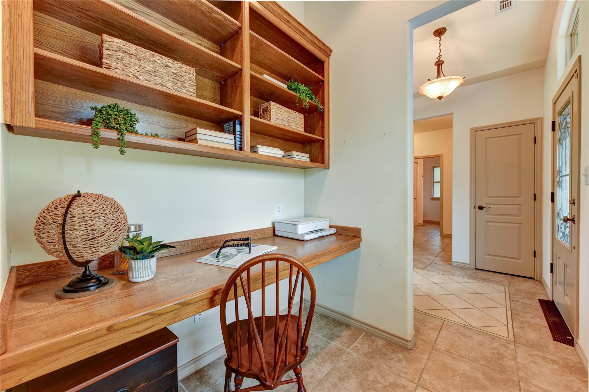 Home office nook with built-in wooden desk and shelving beside a tiled entry hall.
