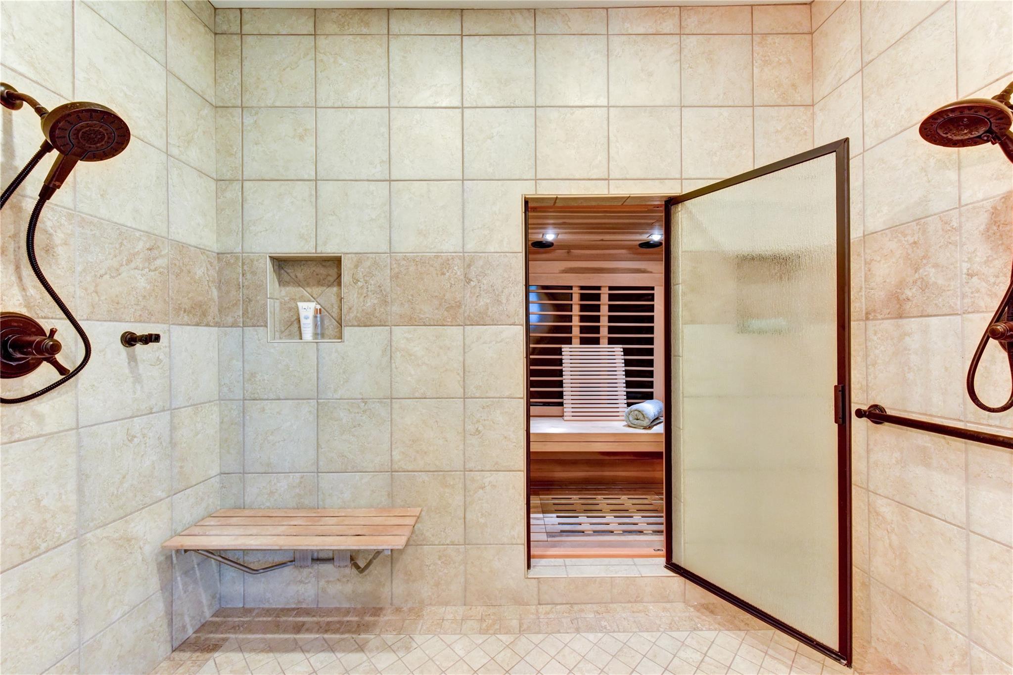 Tiled shower room with a wooden bench and an open doorway to a wood-lined sauna.