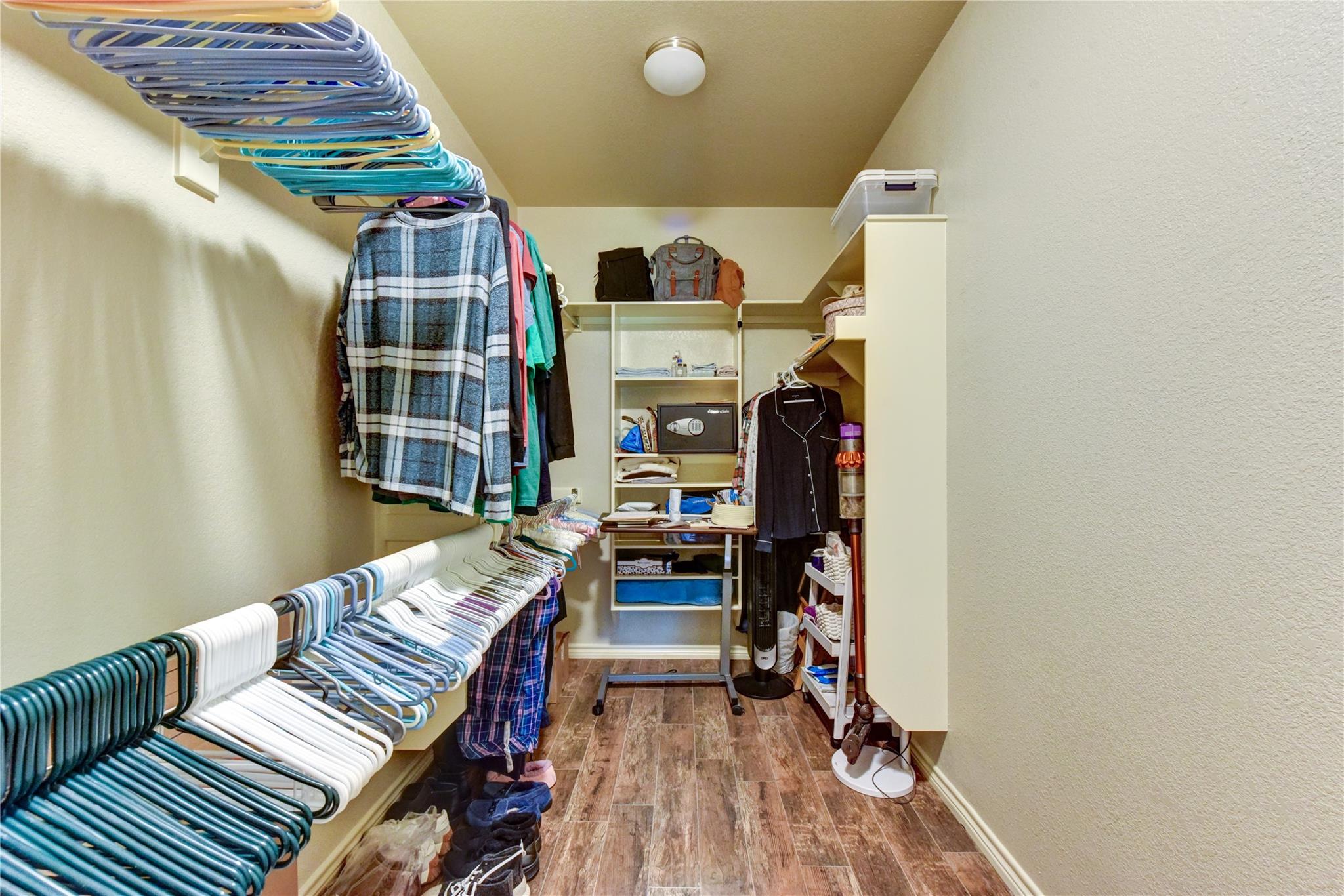 Walk-in closet with built-in shelving, hanging clothes, and wood-look tile flooring.